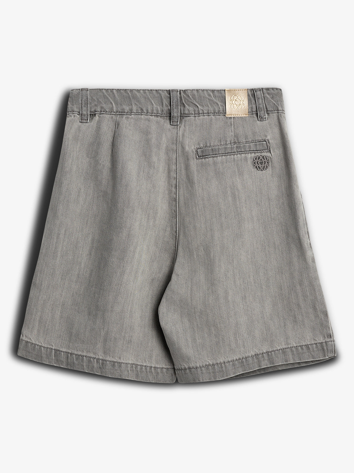 Grå shorts med en enkelt baglomme og bæltestropper; et lyst mærke med logo og broderet emblem. Hængende mod en neutral, lysegrå baggrund.