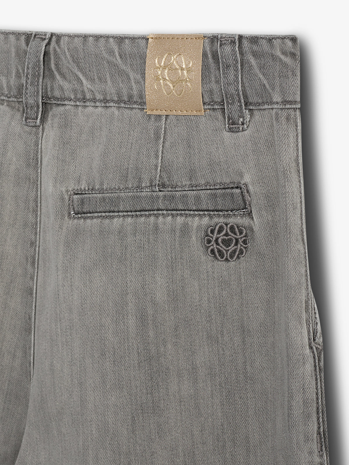 Grå denim bukser med en lomme og broderet logo på lædermærke ved linningen. Baggrunden er en neutral hvid overflade.