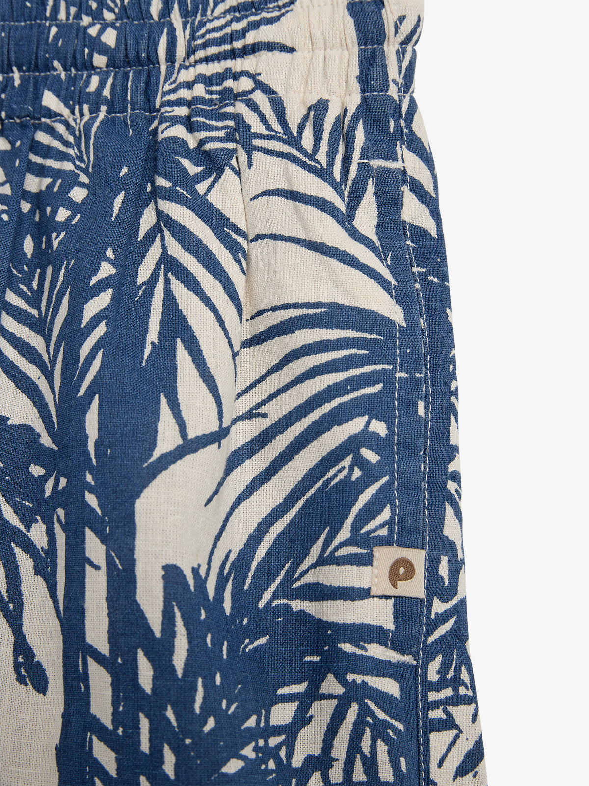 Blue shorts display a white leaf pattern, featuring an elastic waistband and a small brown tag with a "p" logo. The context is plain, focusing on textile design.