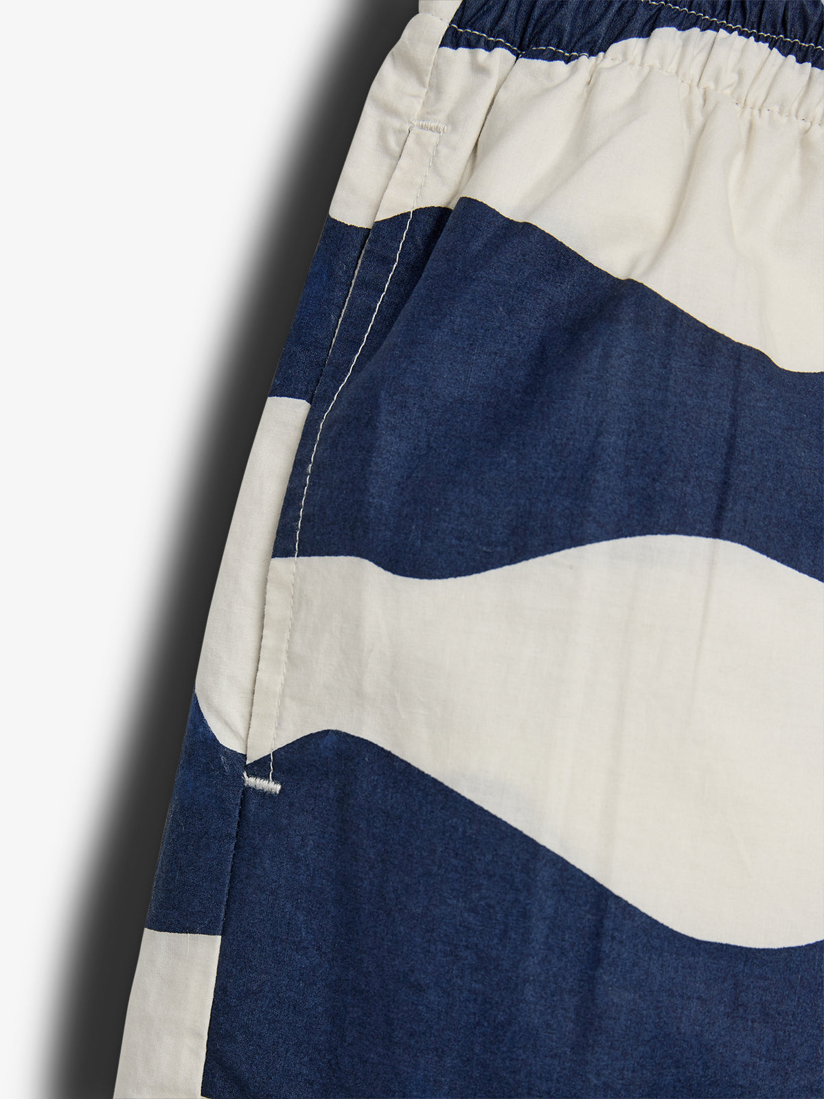 Buksedelen har brede, bølgende, blå-hvide striber og en elastisk talje, der antyder komfort. Stoffet er tæt synet, hvilket giver en robust følelse i et enkelt, minimalistisk design.