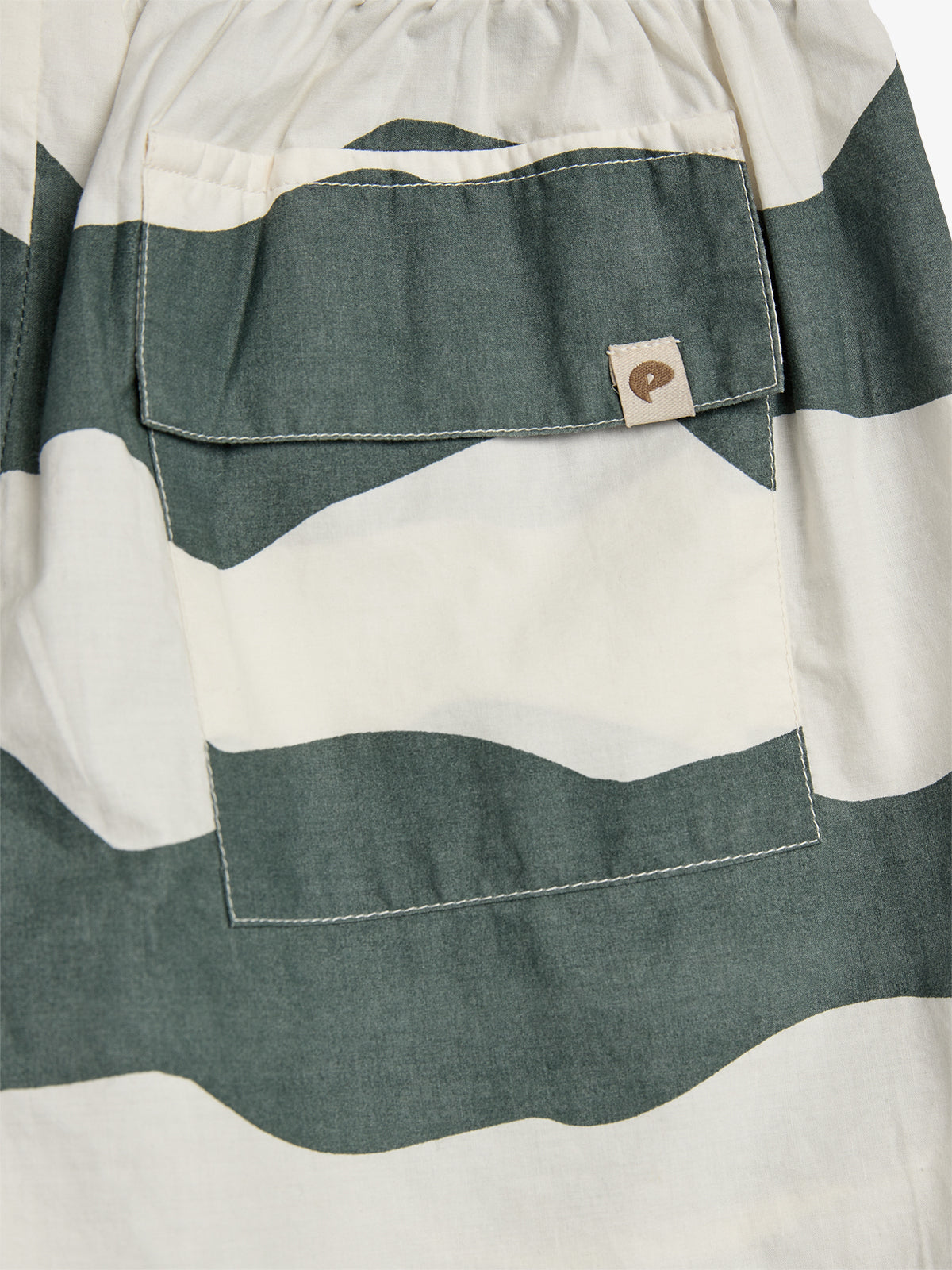 A fabric with wavy green and white patterns features a pocket with a flap. A small tag showing a brown logo resembling a "C" is attached to the pocket.
