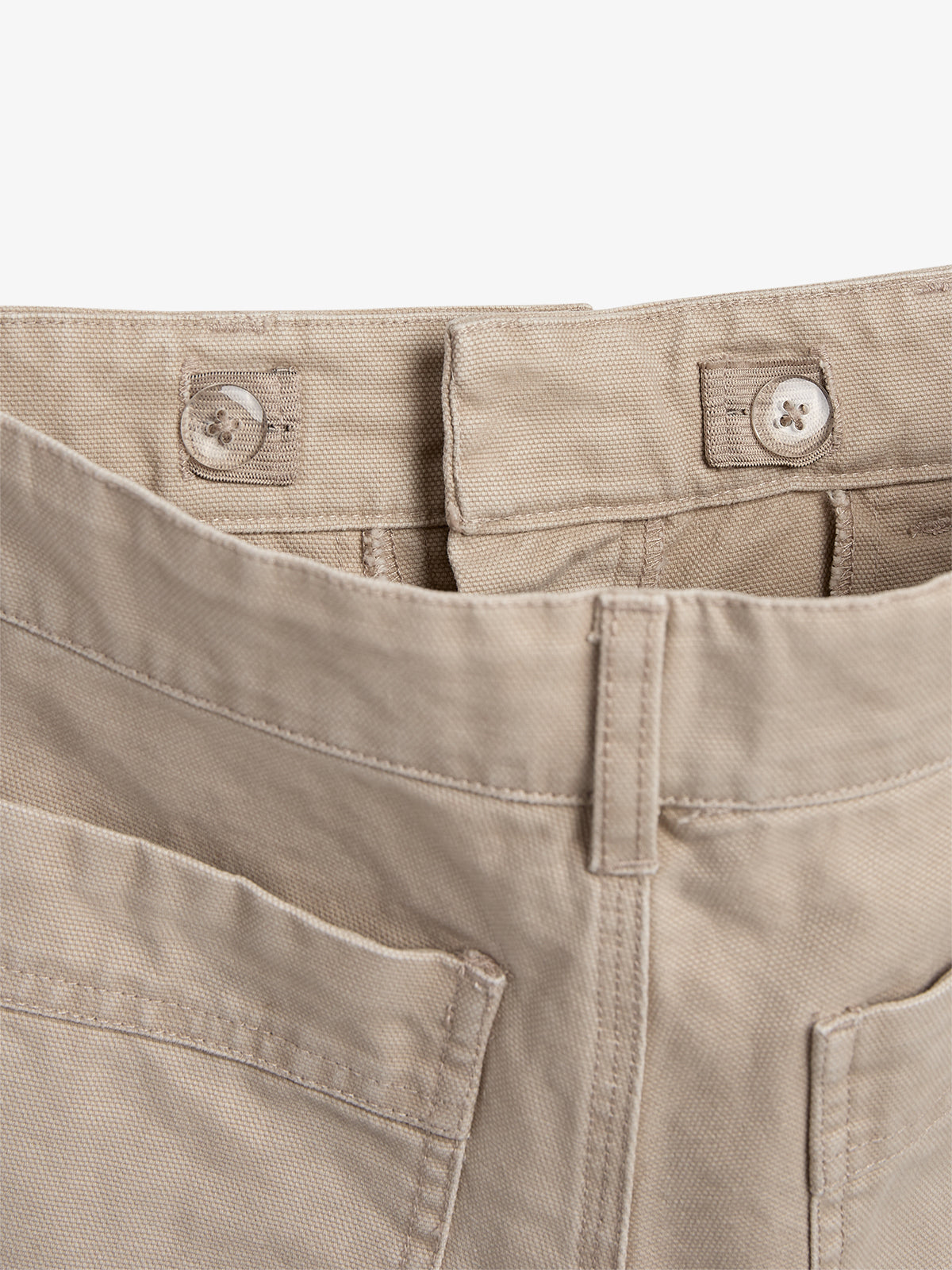 Beige pants waistband with buttoned adjustable tabs, partially open, set against a plain white background.