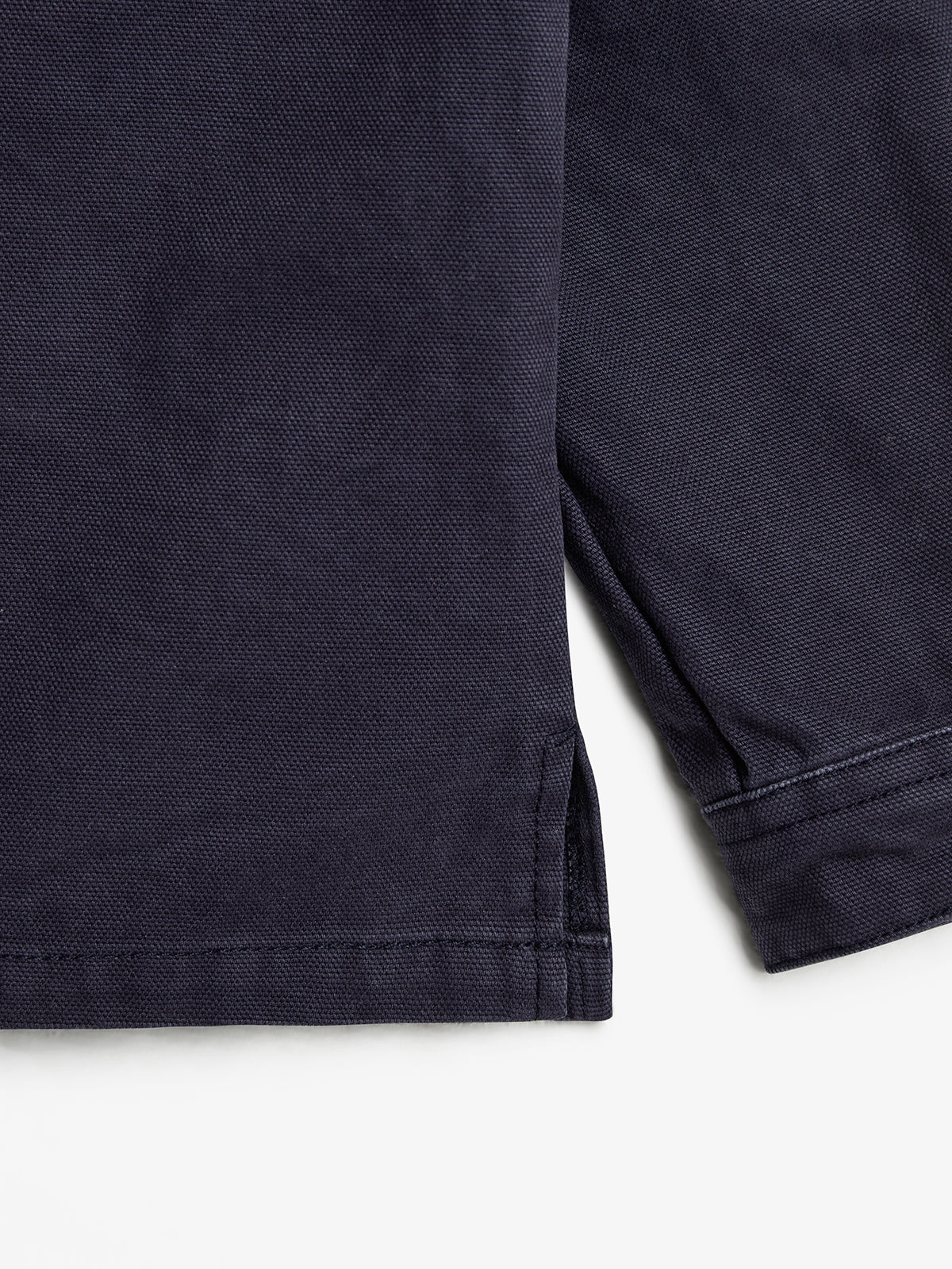 A close-up of a navy blue fabric with visible texture, showing the hem and a side slit seam, laid against a plain white background.