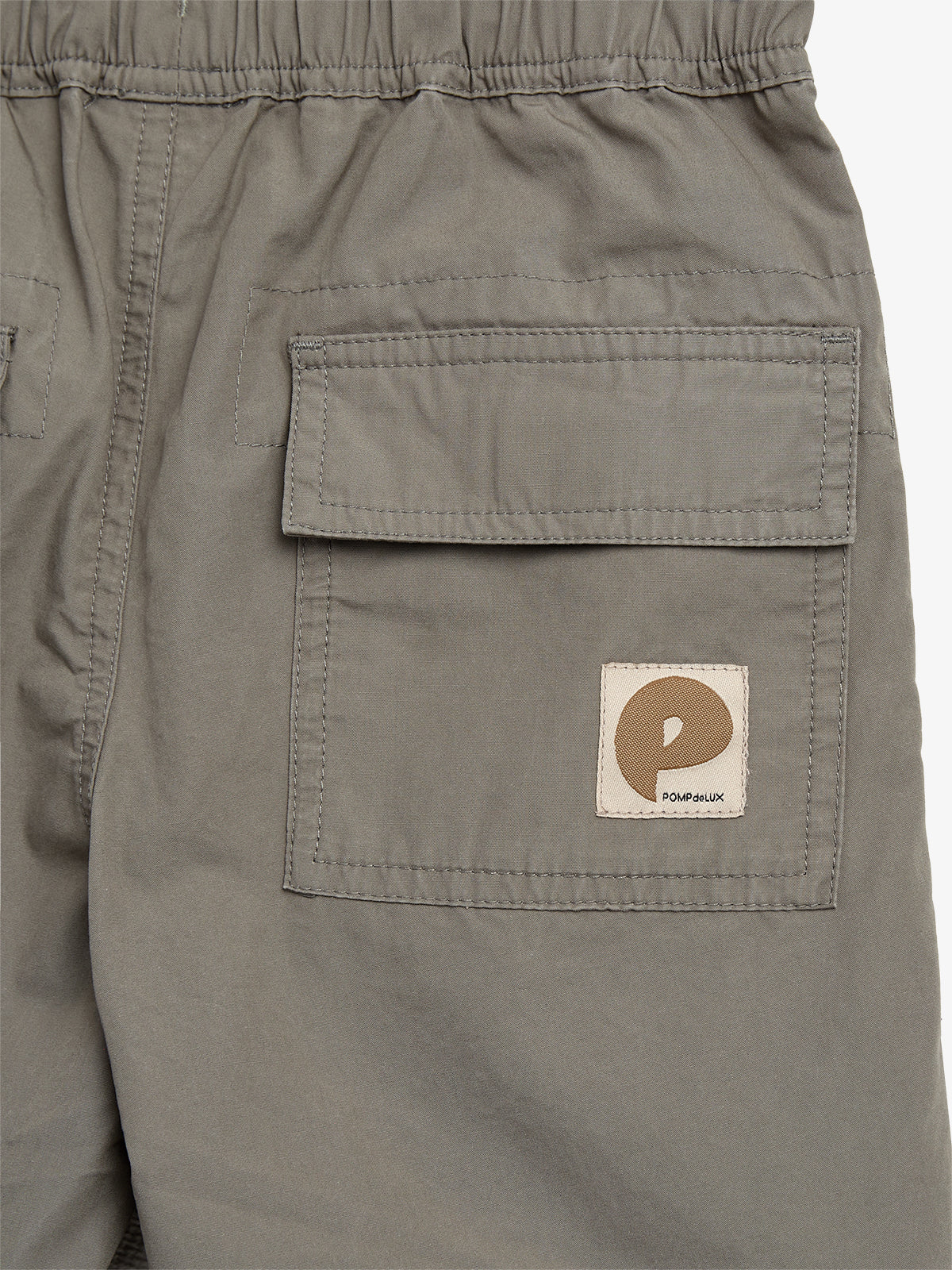 Grå shorts med en lomme og elastisk talje. Lommen har en klap og en logo med teksten "POMPdeLUX". Shortsene er enkle og afslappede i stil.