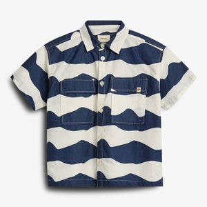 Kortærmet skjorte med brede, bølgende blå og hvide striber. Skjorten har to brystlommer og hvide knapper. Baggrund er ensfarvet hvid.