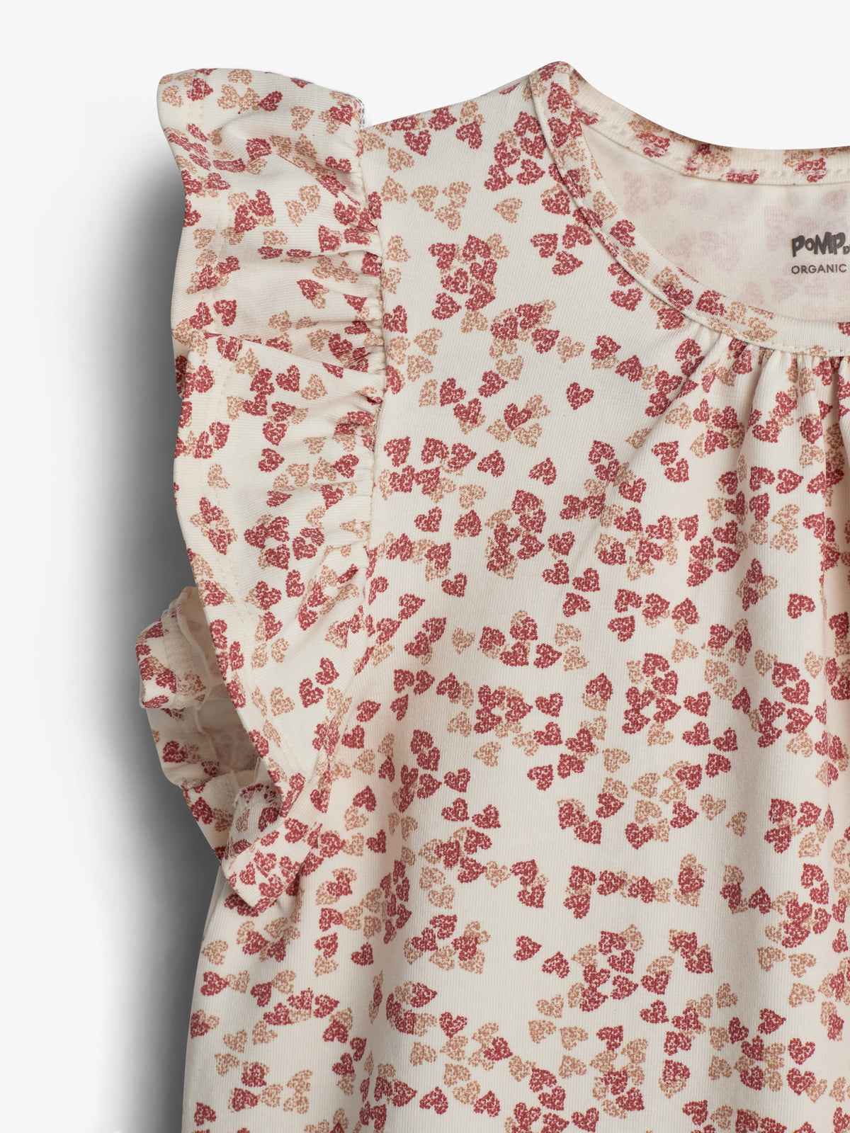 Bluse med små blomstertryk i røde nuancer, har korte flæseærmer. Tekst ved halsudskæringen: "POMPdeLUX ORGANIC". Baggrunden er en ensfarvet, neutral tone.