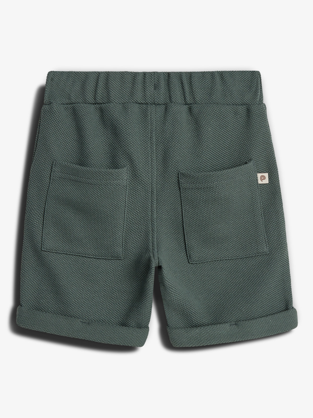 Grønne shorts med elastisk talje og to firkantede lommer bagpå. Stoffet er tekstureret, og der er et lille mærke på siden. Baggrunden er hvid.