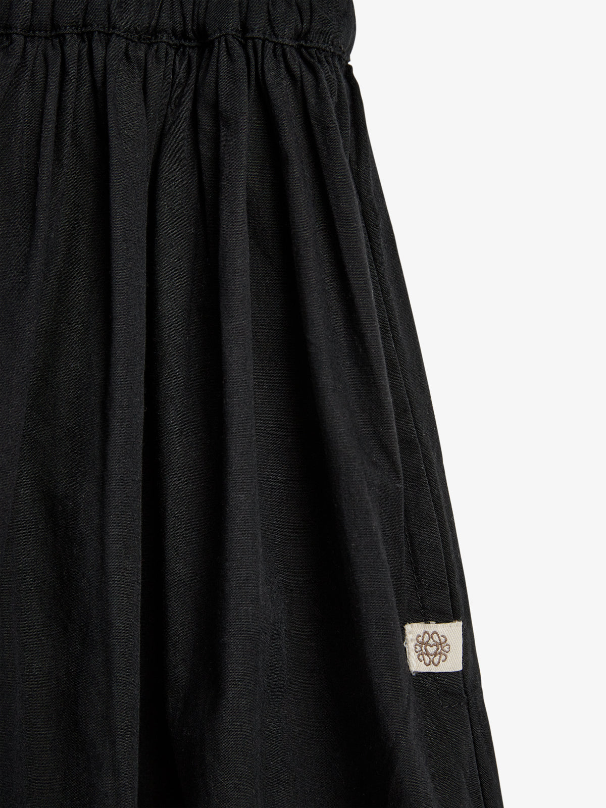 A black gathered fabric skirt features a small, white tag with a decorative symbol, set against a plain white background.
