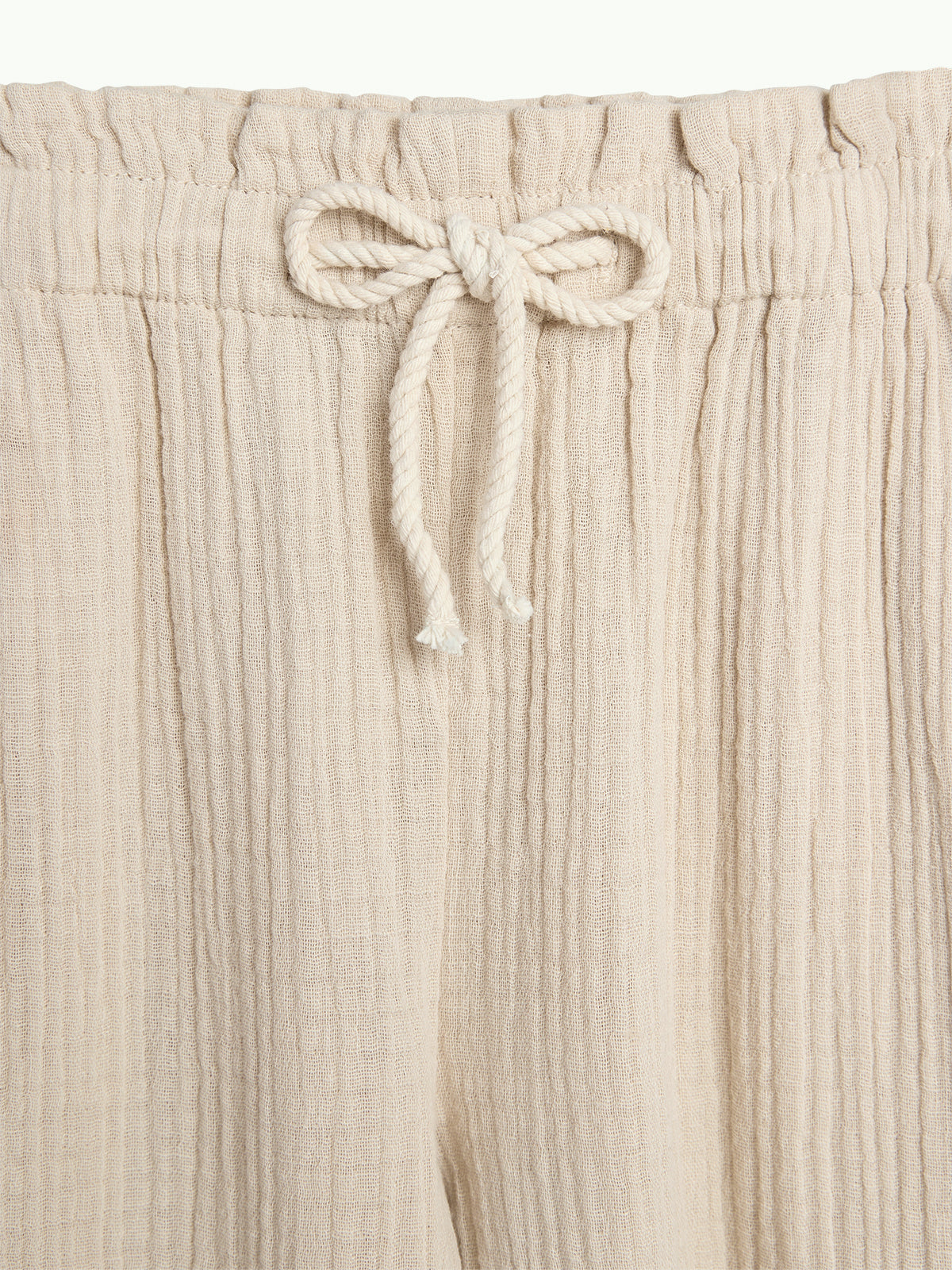 Beige crinkled fabric pants with an elastic waist feature a tied rope drawstring, creating a casual look against a plain background.