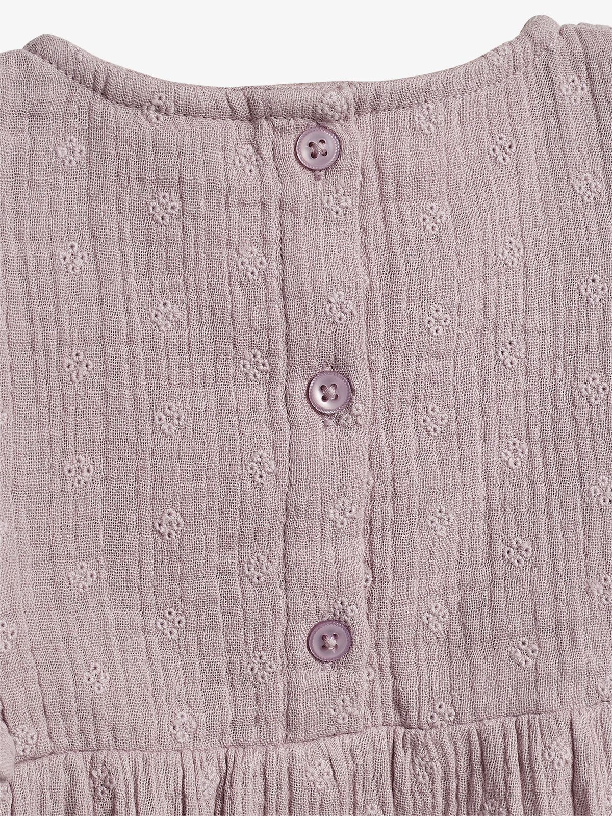 Pink textured fabric with small floral patterns features three purple buttons in a vertical line. The material is gently gathered at the bottom, suggesting it's part of a garment.