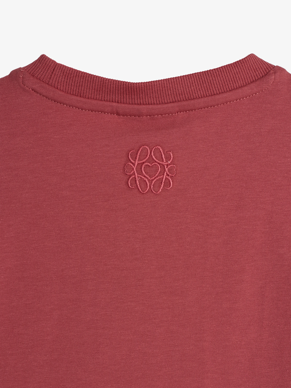 A red sweatshirt features an embroidered logo on the back below the ribbed neckline. The fabric appears soft, with a minimalist design against a plain background.