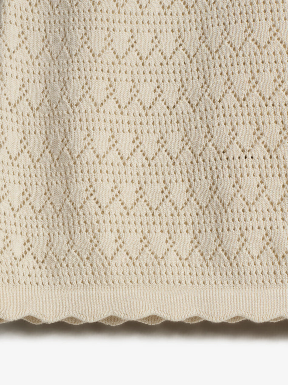 A knitted fabric features a diamond lace pattern, creating a textured design. The edge is scalloped, adding a decorative finish. The context suggests a close-up view.