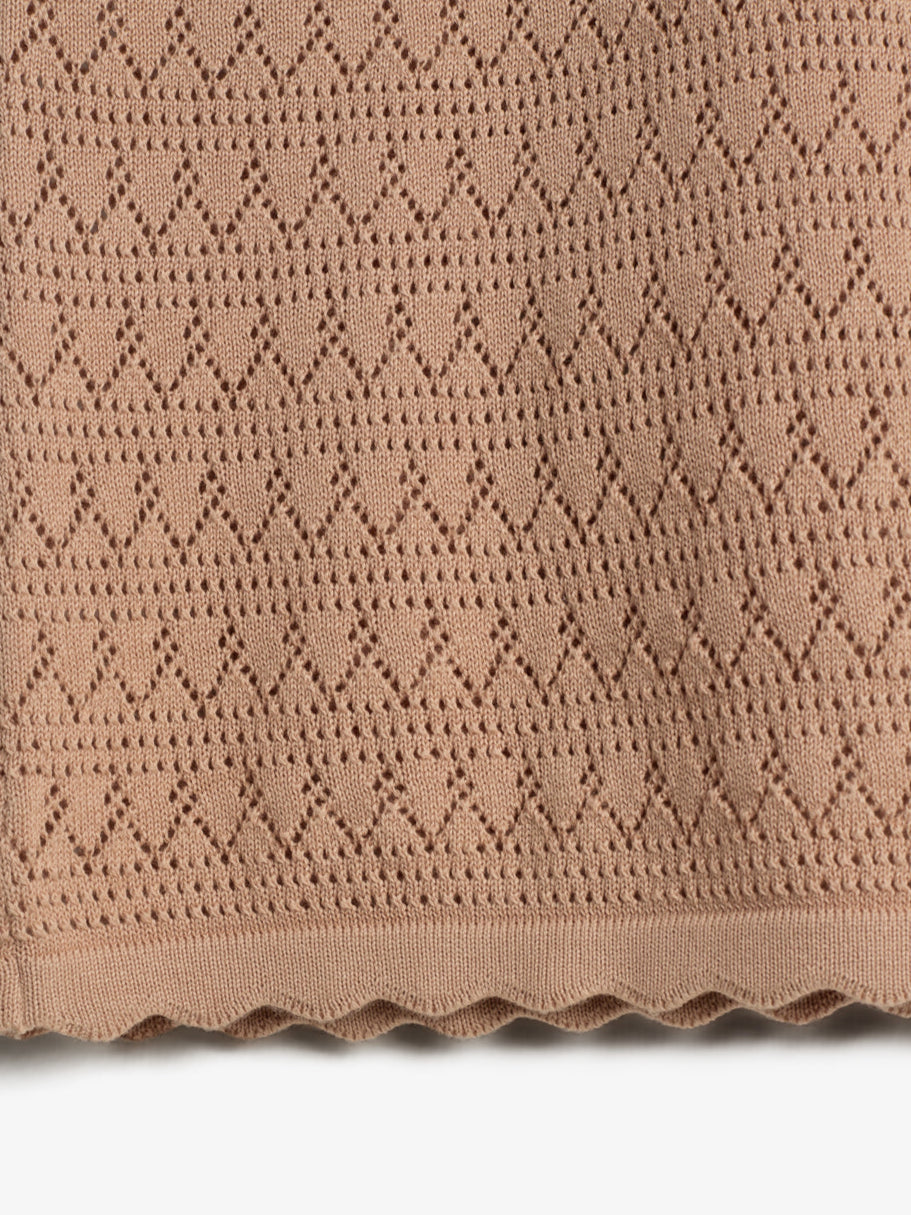 Beige knitted fabric with a repeating diamond pattern, scalloped edge. Close-up view, displaying intricate openwork design on a flat surface.