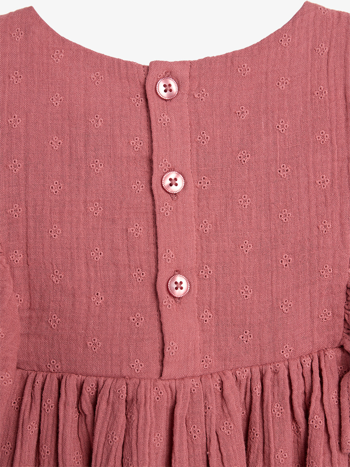 A textured pink dress has three matching buttons down the back. The fabric features small, repeating floral patterns, and the bottom section is gathered, creating a soft, pleated effect.
