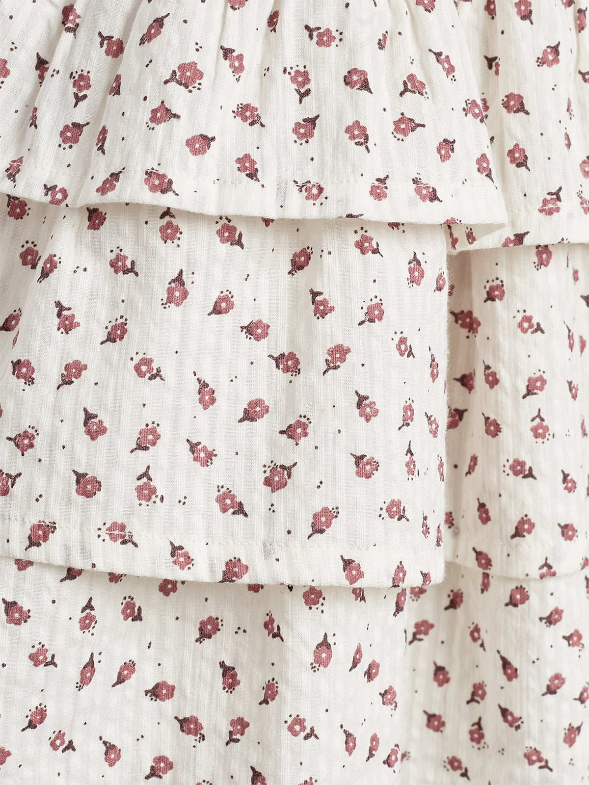 White ruffled fabric features a pattern of small, scattered red flowers. The material is layered, adding texture and depth to the design.