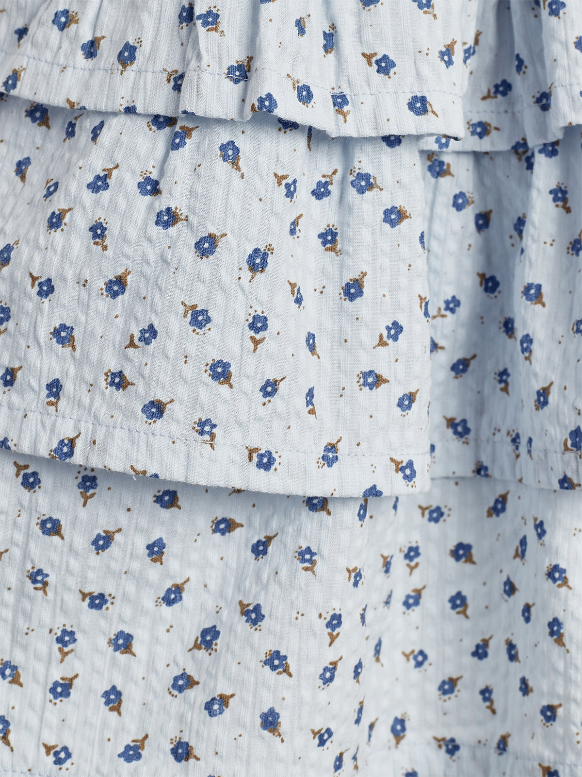 Fabric displays a pattern of small blue flowers with brown accents, arranged uniformly on a light background. The texture appears slightly crinkled, creating a layered, flowing effect.