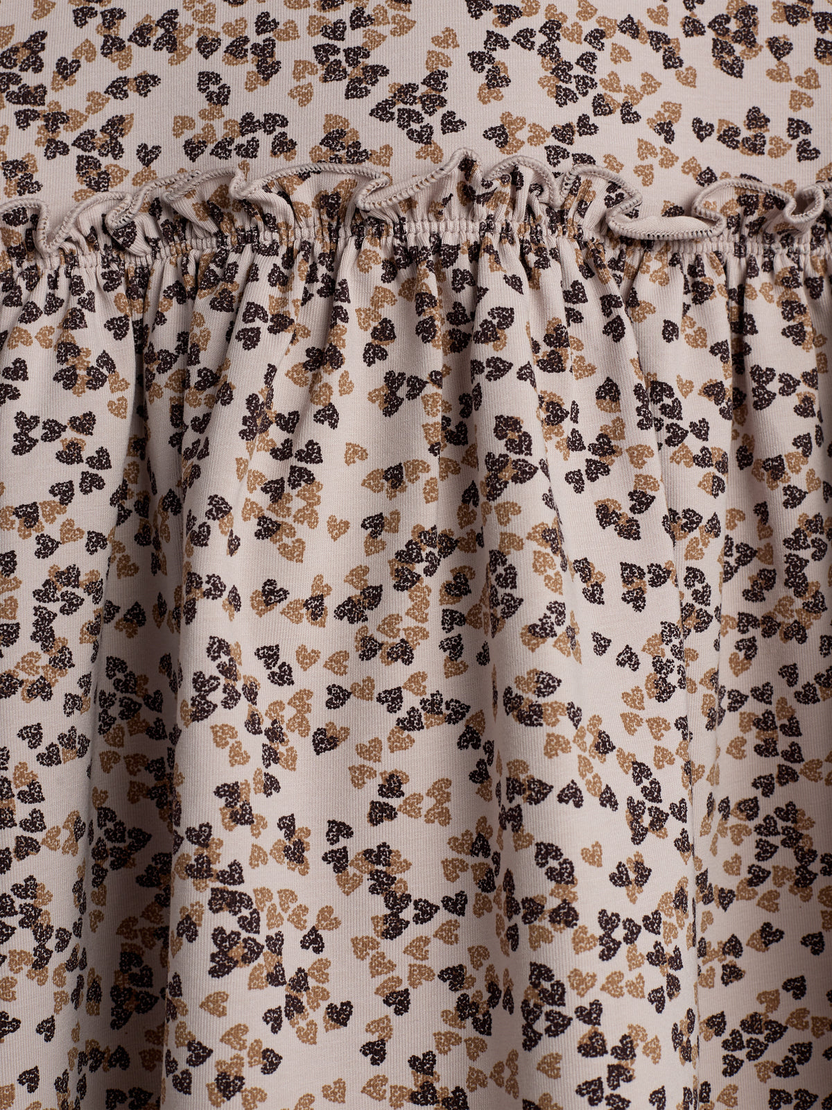 Stof med blomsterprint, rynket i en elastisk syning, skaber en flæsedetalje. Farverne er beige, sort og brun, hvilket giver et naturligt look.