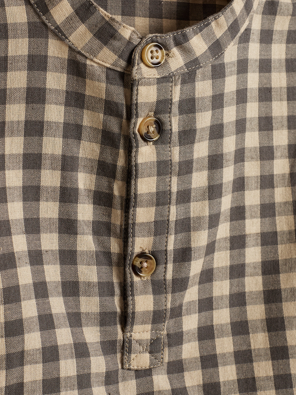 Skjorte med ternet mønster viser tre knapper på en lodret række. Stof i beige og sort danner små firkantede tern. Stoffet er let krøllet og uden tekst.
