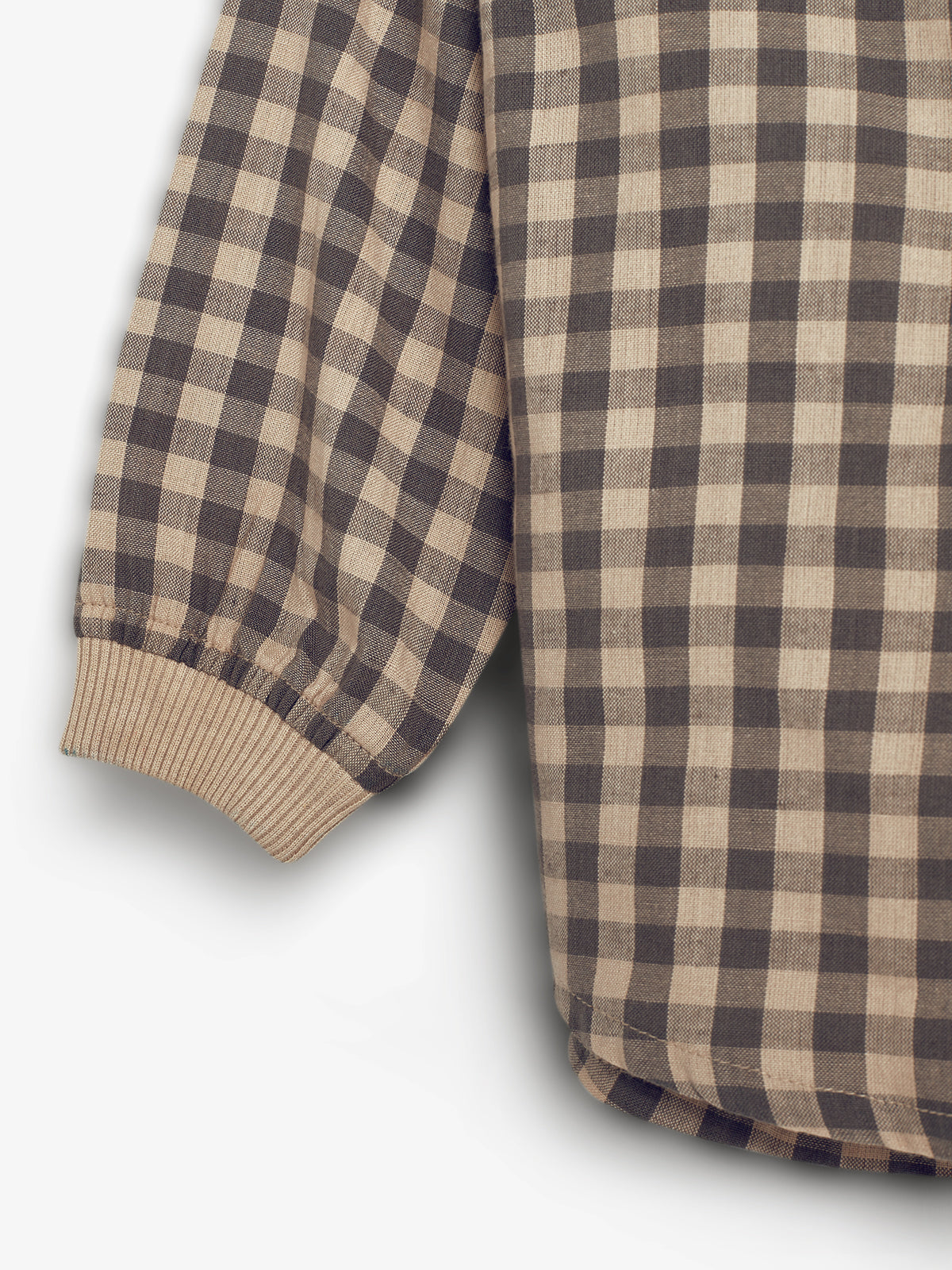 Skjorte med ternet mønster, har en ribbet manchet. Stoffet er i en kombination af beige og mørkebrune firkanter, ligger på en lys baggrund.
