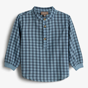 Skjorte i blåternet mønster hænger mod en ensfarvet baggrund. Skjorten har en krave og tre knapper foran. Teksten på mærket siger "POMP DE LUX, 86 cm".