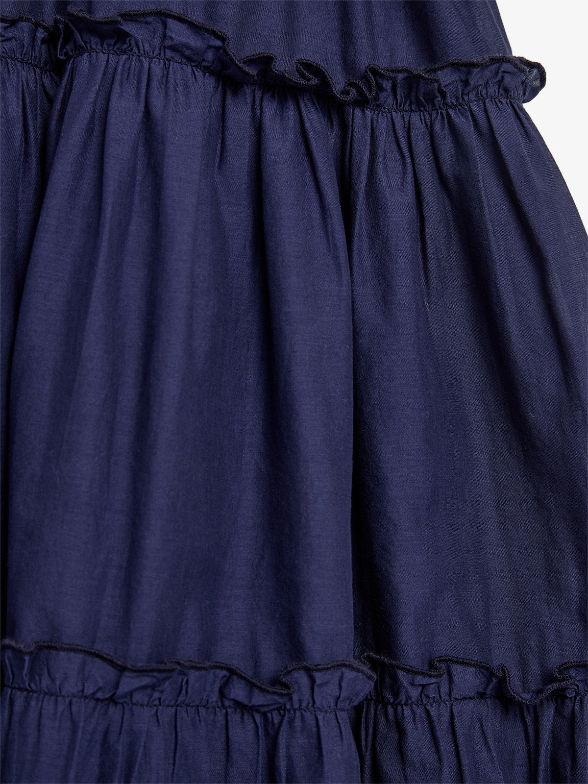 A navy blue, tiered fabric with ruffled trim overlaps, creating a textured appearance; the close-up shot emphasizes fabric structure, devoid of background context.