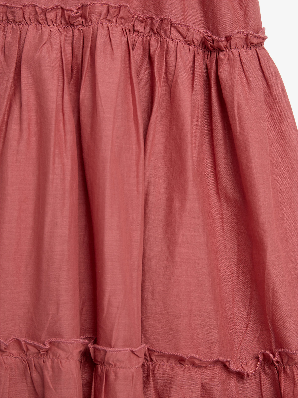 Ruffled layers of maroon fabric hang vertically, showcasing gathered stitching, creating a textured, flowing appearance in a close-up view. The background is plain white.