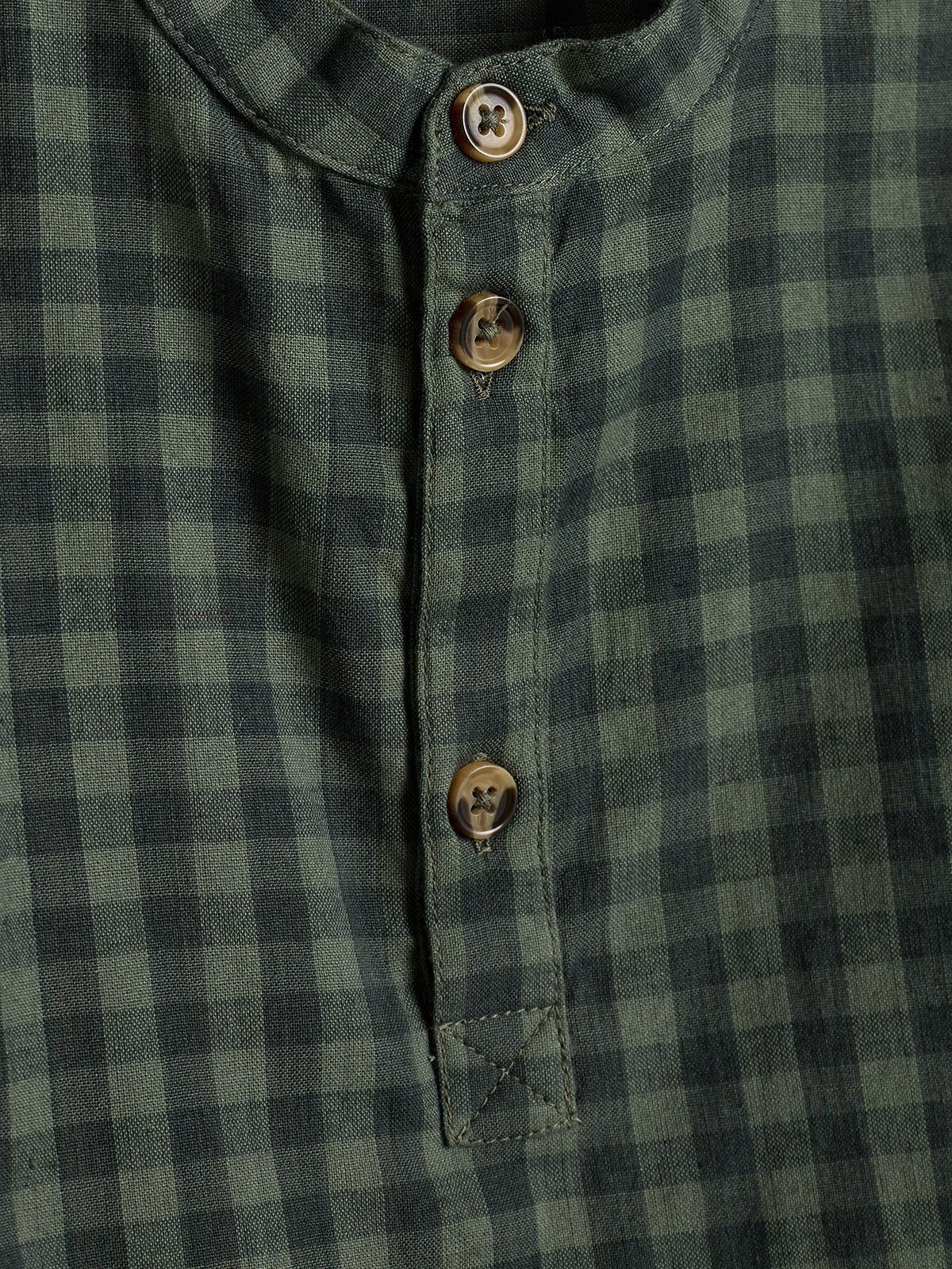 Skjorte med grøn- og sortternet mønster; tre brune knapper langs åbningen. Stoffet har en afslappet tekstur og flad krave, egnet til uformelle anledninger.