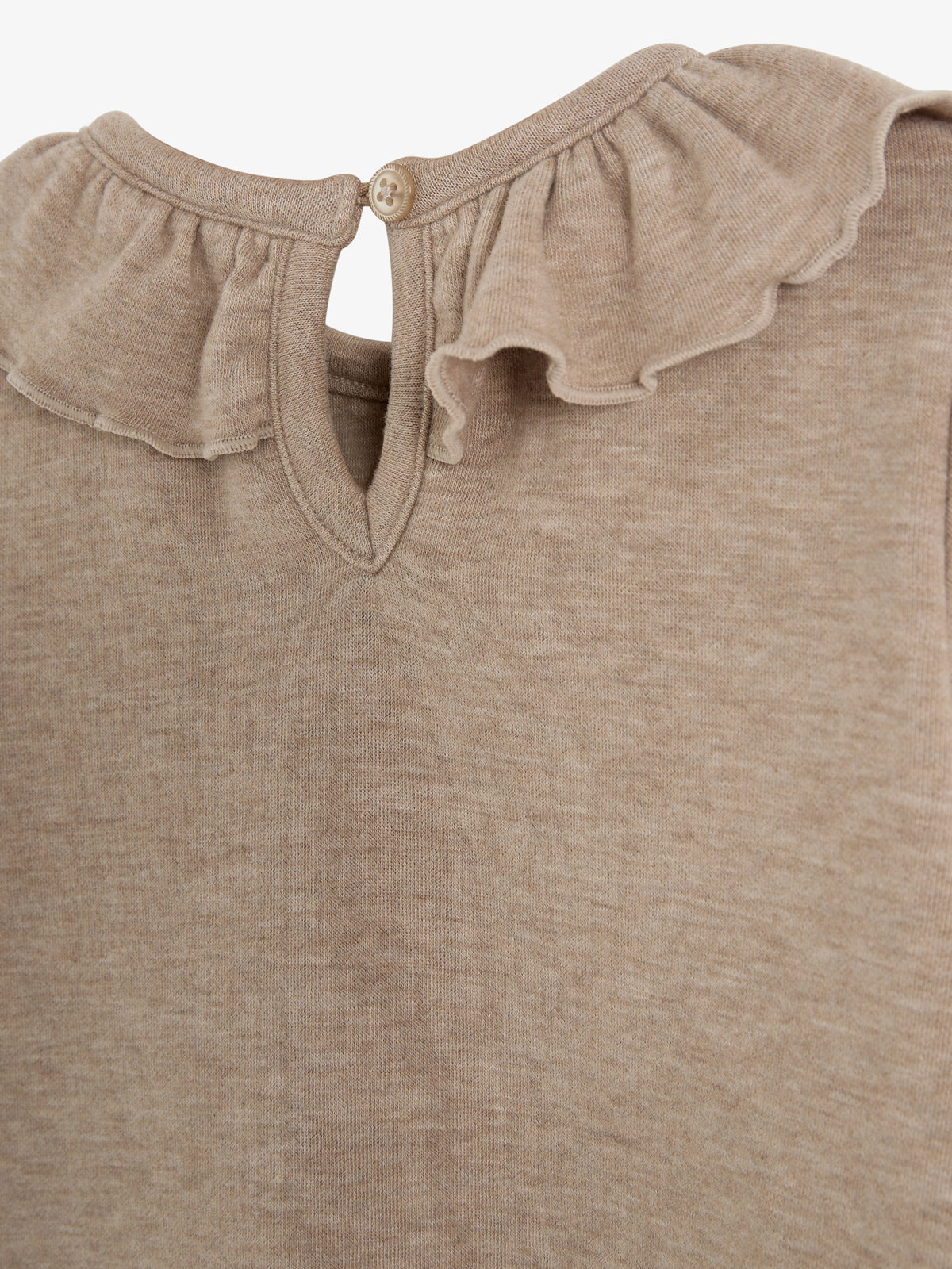 Beige bluse i nærbillede; har en knaplukning bagpå med en lille flæsekant rundt om halsen og en jævn tekstur, som fremhæver en enkel, elegant stil.