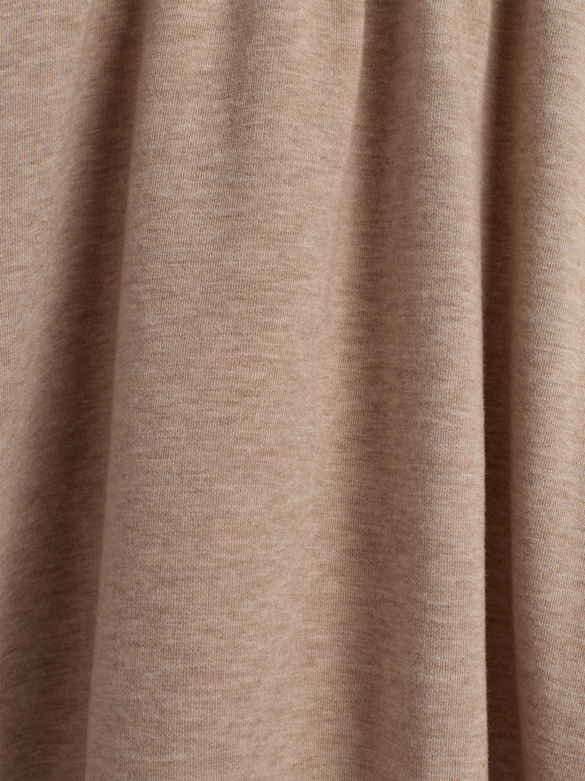 Beige stof hænger i bløde folder, der skaber en lige og glat struktur. Det ser ud til at være en del af et større tekstil, muligvis beklædning eller gardin.