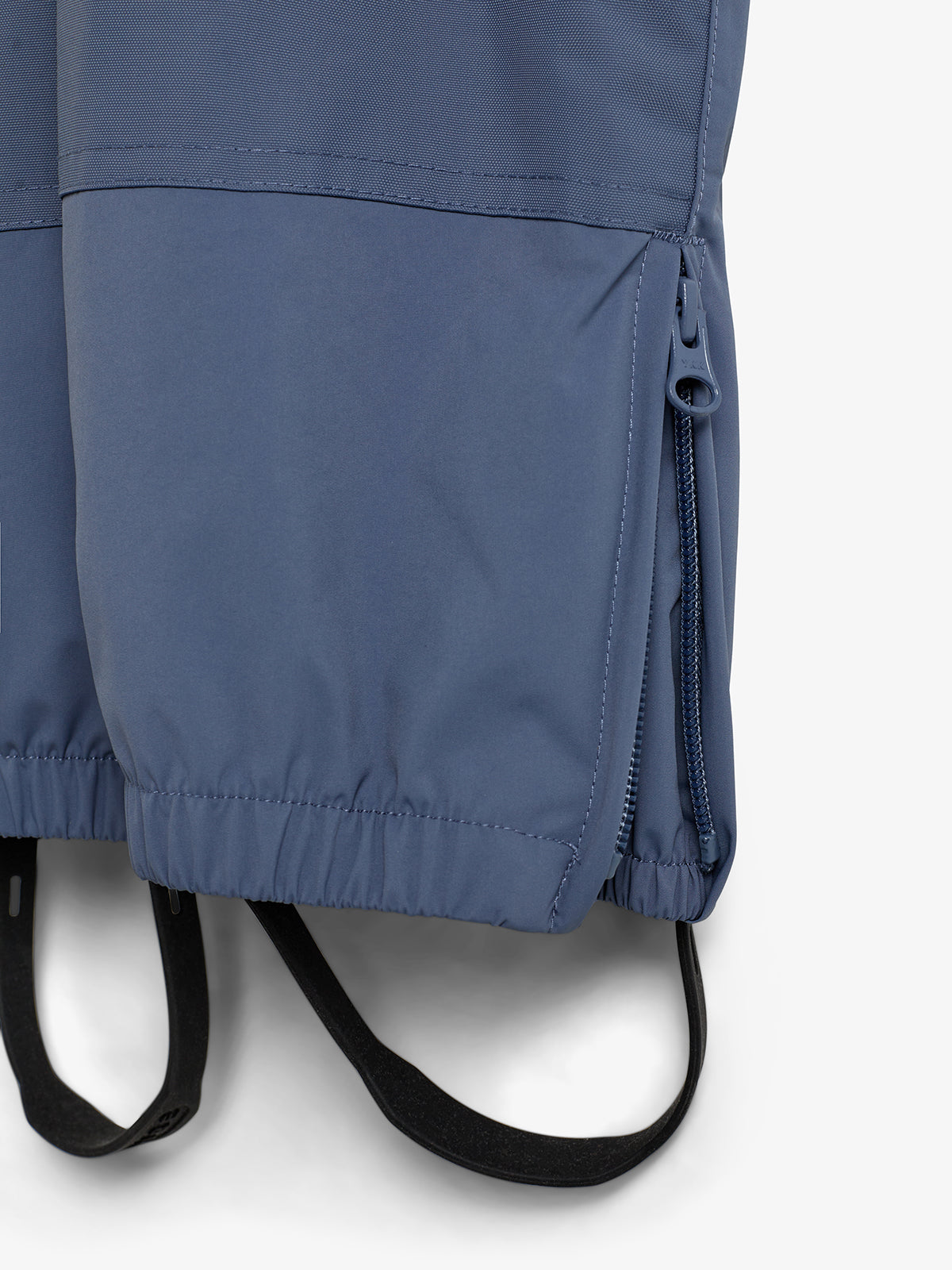 Blåt vandtæt stof med lynlås i siden, elastisk kant nederst og sorte elastiske stropper. Stoffet er syet i paneler, ses mod en neutral, lys baggrund.