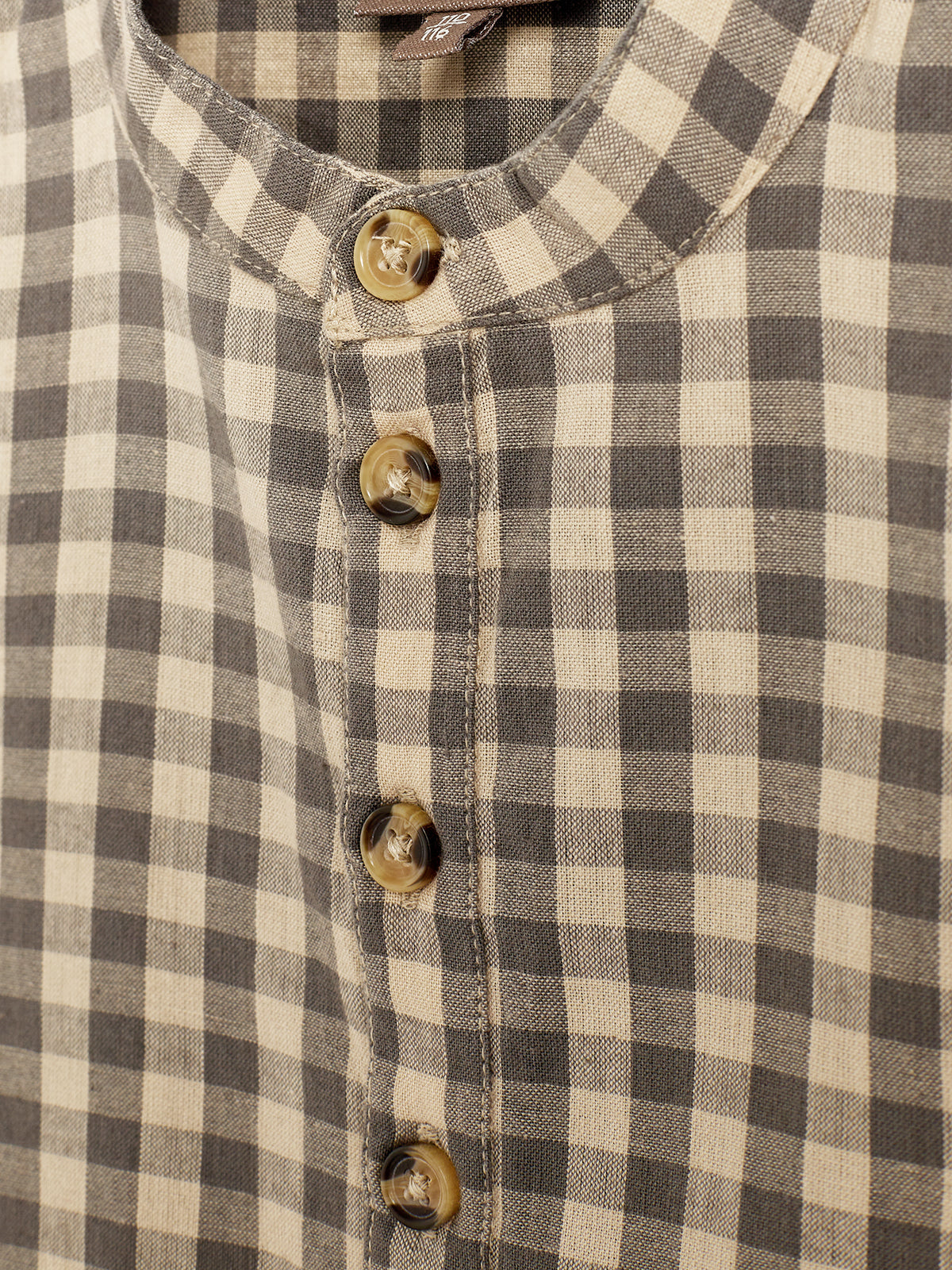 En skjorte med ternet mønster i beige og grå nuancer har en række brune knapper langs midten. Stoffet er let struktureret og syningen er tydelig.