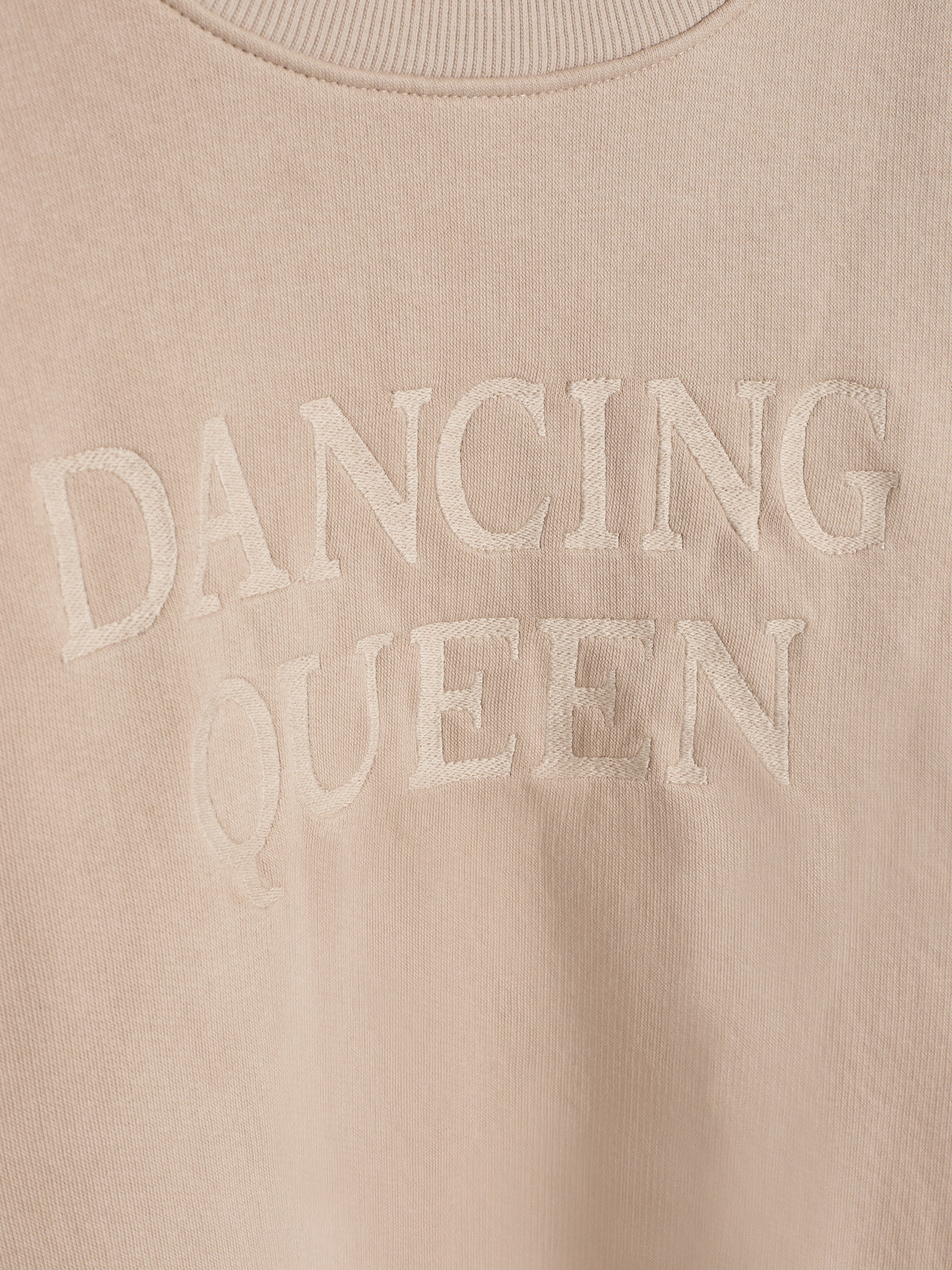 Beige sweatshirt med teksten "DANCING QUEEN" broderet på brystet, placeret i en neutral baggrund uden andre objekter eller elementer.