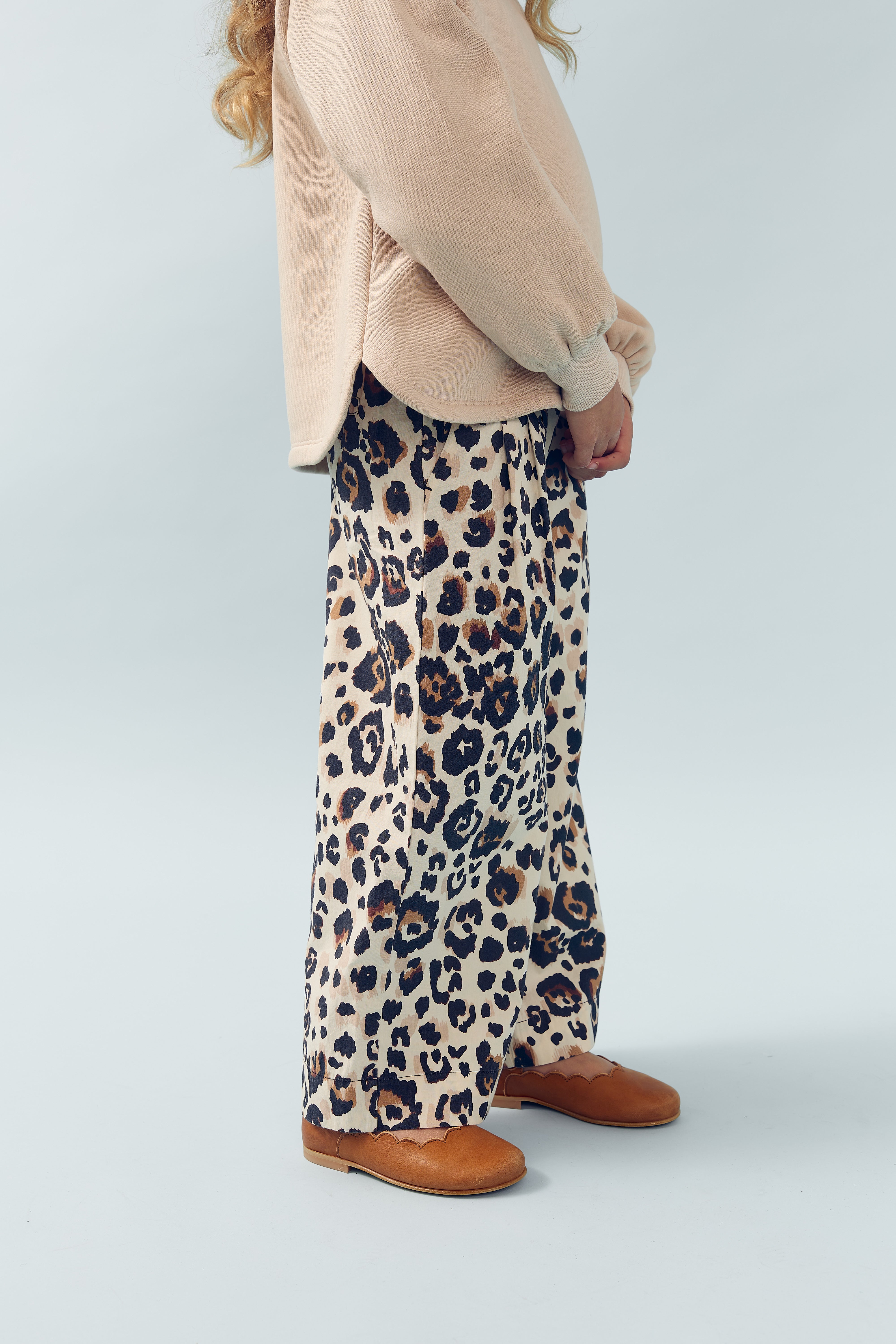 Skørt med leopardmønster bæres af en person iført en lyserød trøje og brune sko. Personen står indendørs mod en lys baggrund.