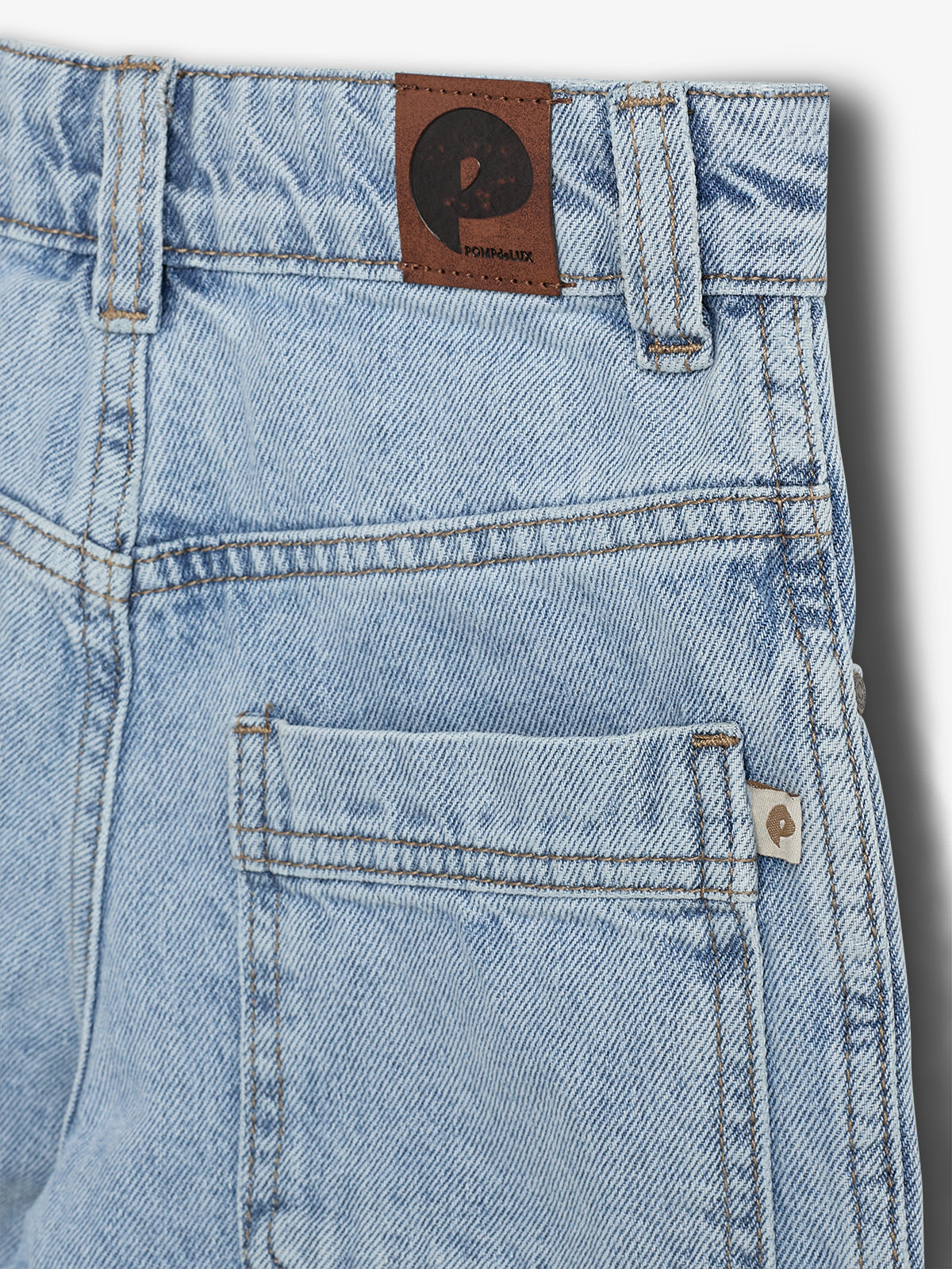 Jeans i lys denim med en lædermærkat med bogstavet "P" og teksten "POMPADOUR". Lommer og bæltestropper i en almindelig stil, præsenteret mod en neutral baggrund.