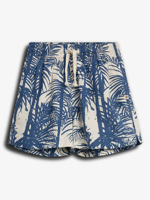 Shorts med et blåt palmemønster, har en beige snøre, der giver en afslappet strandstil. Baggrunden er ensfarvet lys grå, hvilket fremhæver shortsene.