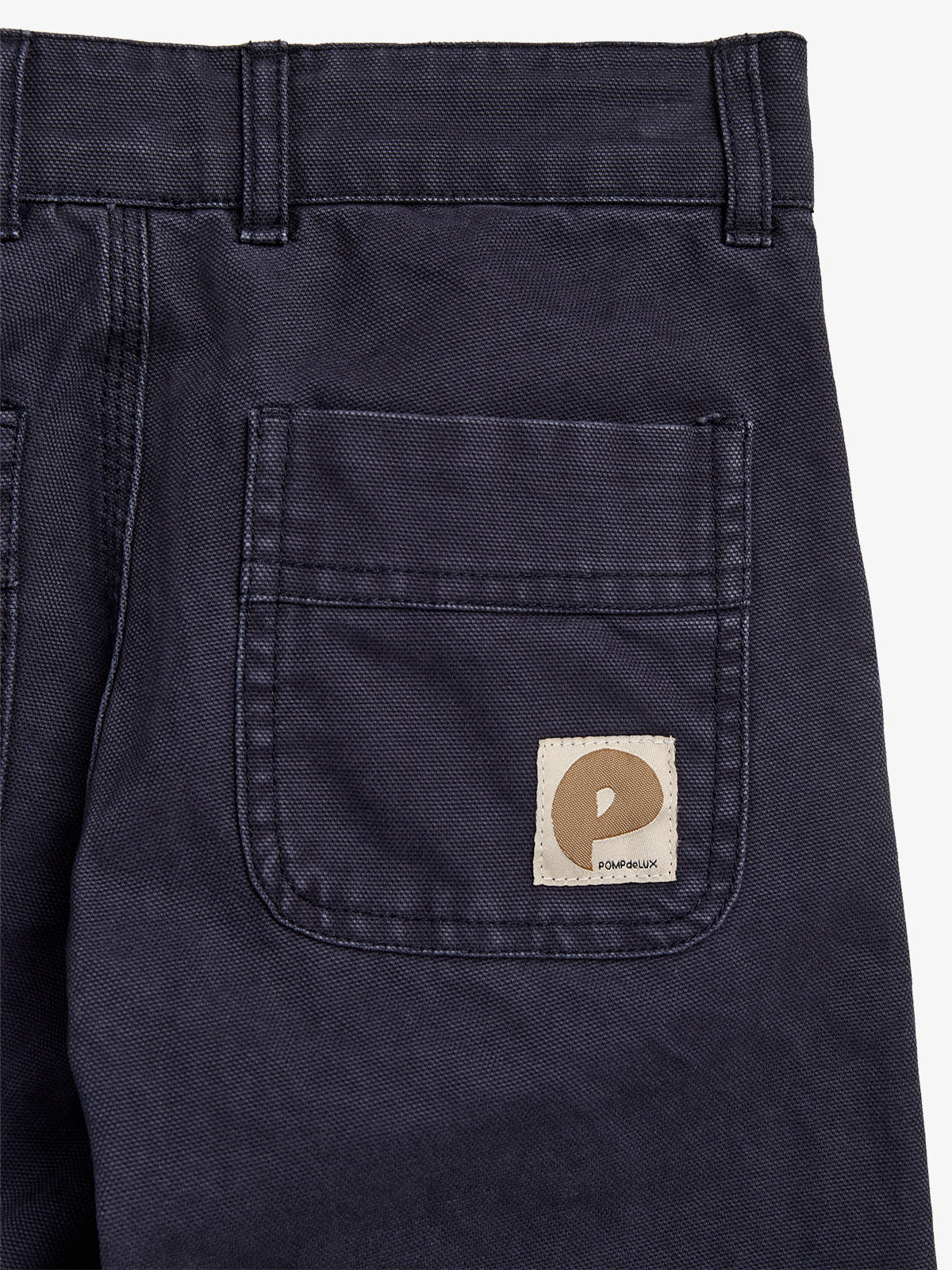 Blue pants feature a back pocket with a beige square patch. The patch displays a brown abstract logo and text: "POMPéLiUX." The pants are in a neutral setting.