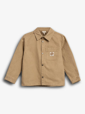 Beige skjorte med krave og lange ærmer, har en knaplukning. På brystet er der en lomme med et firkantet mærke, der viser et bogstav-logo. Baggrund er ensfarvet hvid.