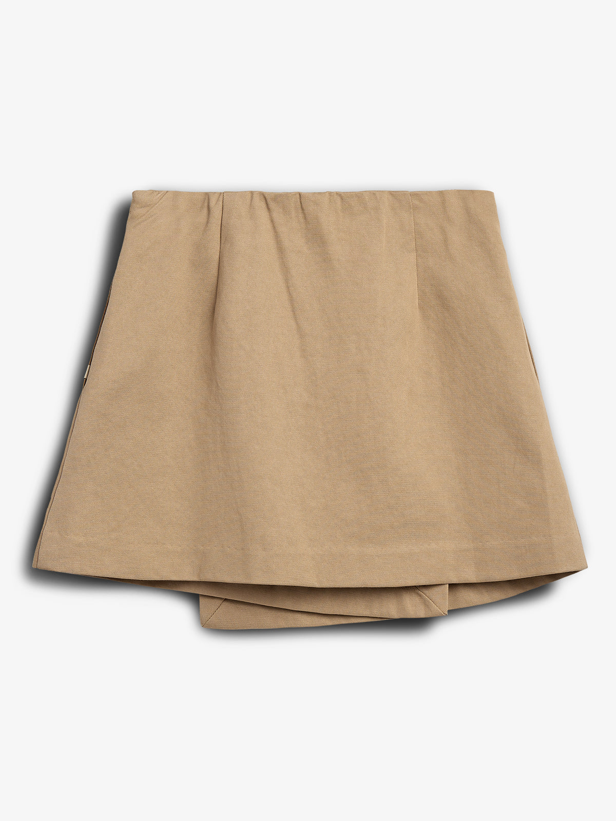 Nederdel i beige farve, ligger fladt foldet; enkel og uden mønster med let rynket talje. Baggrunden er hvid og enkel.