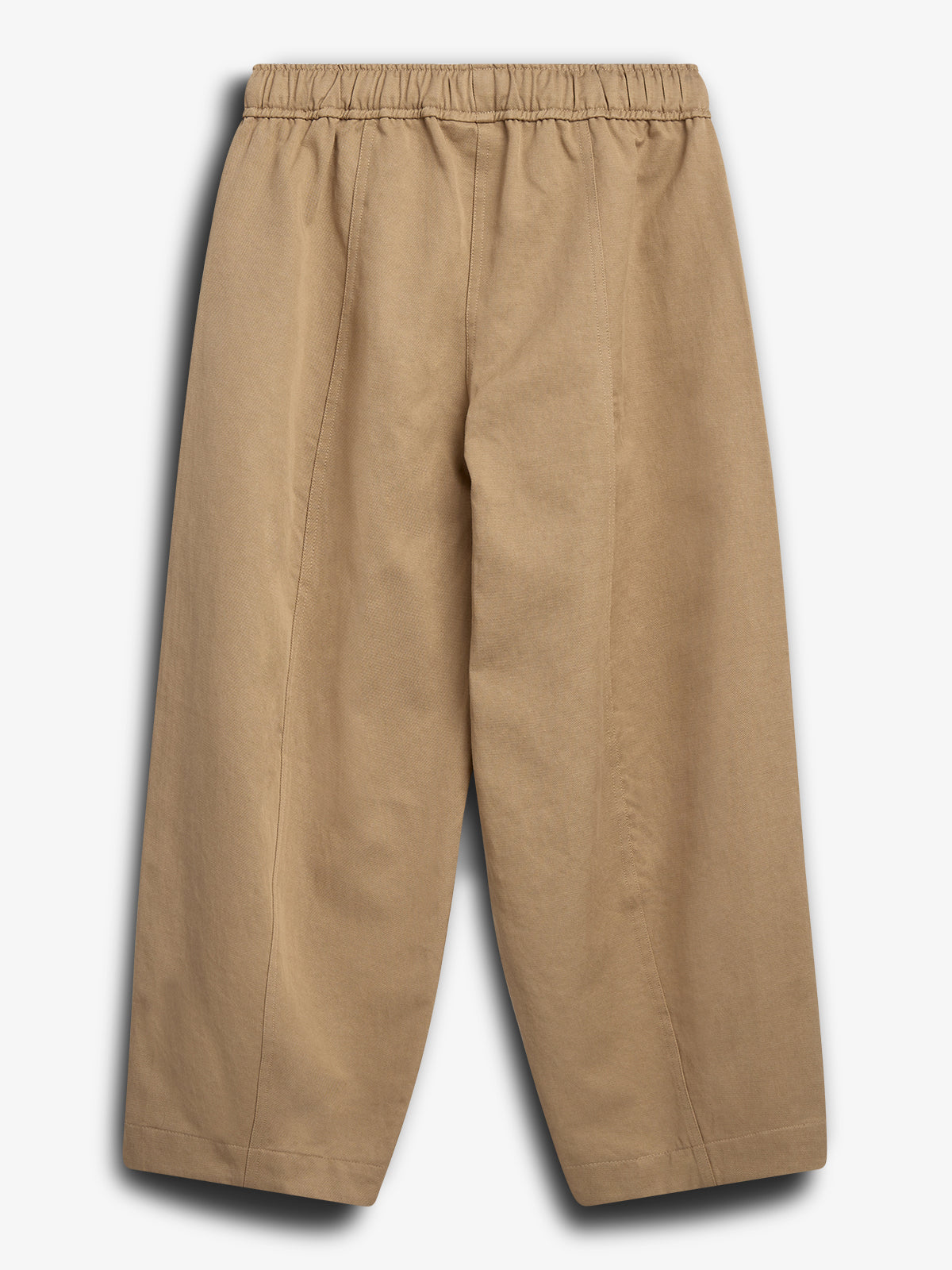 Bukserne er beige med elastisk talje og brede ben, hænger stille imod en hvid baggrund, hvilket skaber et minimalistisk, klart syn.