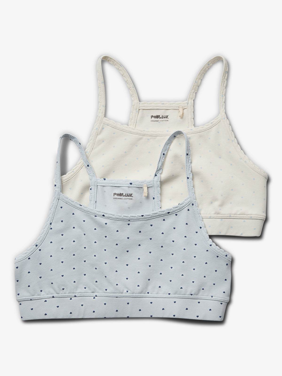 To toppe med stropper ligger ovenpå hinanden; én lyseblå med små hjerter foran, én cremefarvet bagved. Tekst: "POMPdeLUX ORGANIC COTTON" på begge i etiketten.
