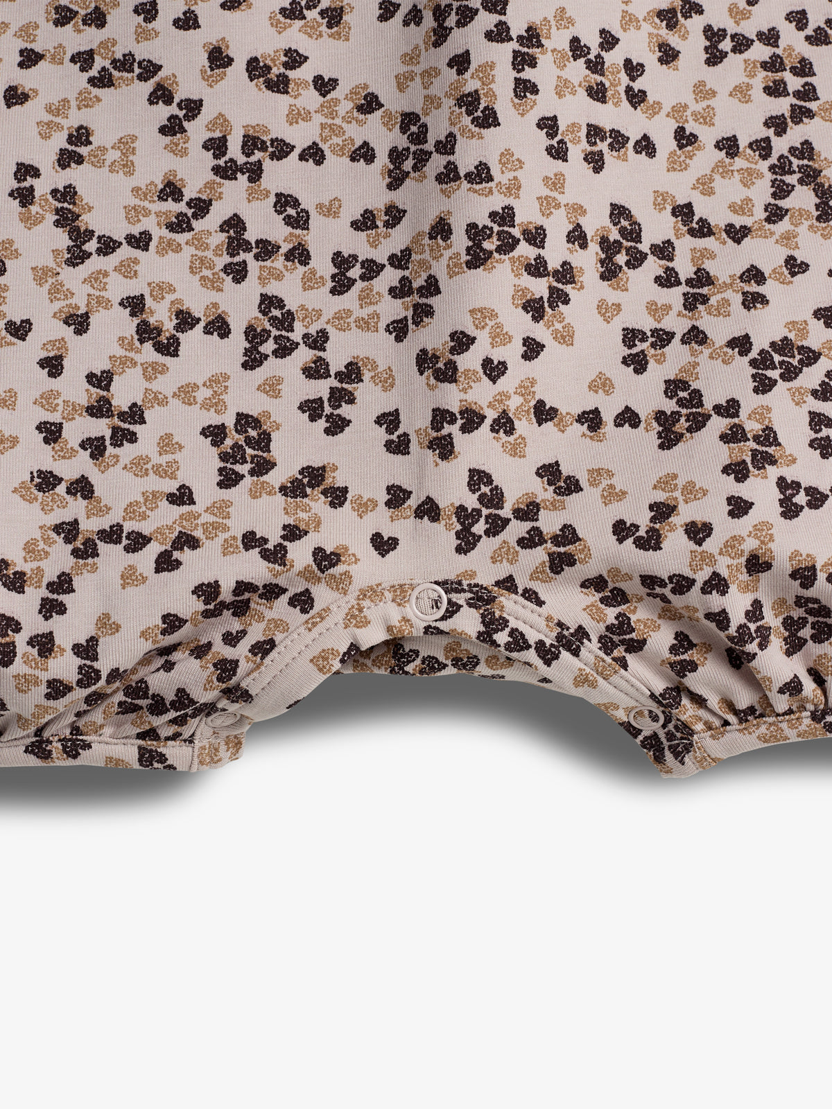 En bluse med små, brune og beige blomstertryk ligger fladt mod en hvid baggrund. To knapper er synlige langs bunden af blusen.