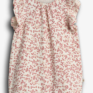 En babyromper med blomsterprint i røde nuancer, har flæser ved skuldrene. Tekst: "PAPU LUX ORGANIC COTTON". Hvid baggrund.