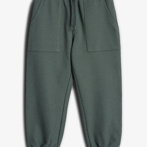 Grønne joggingbukser med elastiklinning og snøre, ligger fladt mod en hvid baggrund. Bukserne har to forlommer og elastisk manchetter ved anklerne.