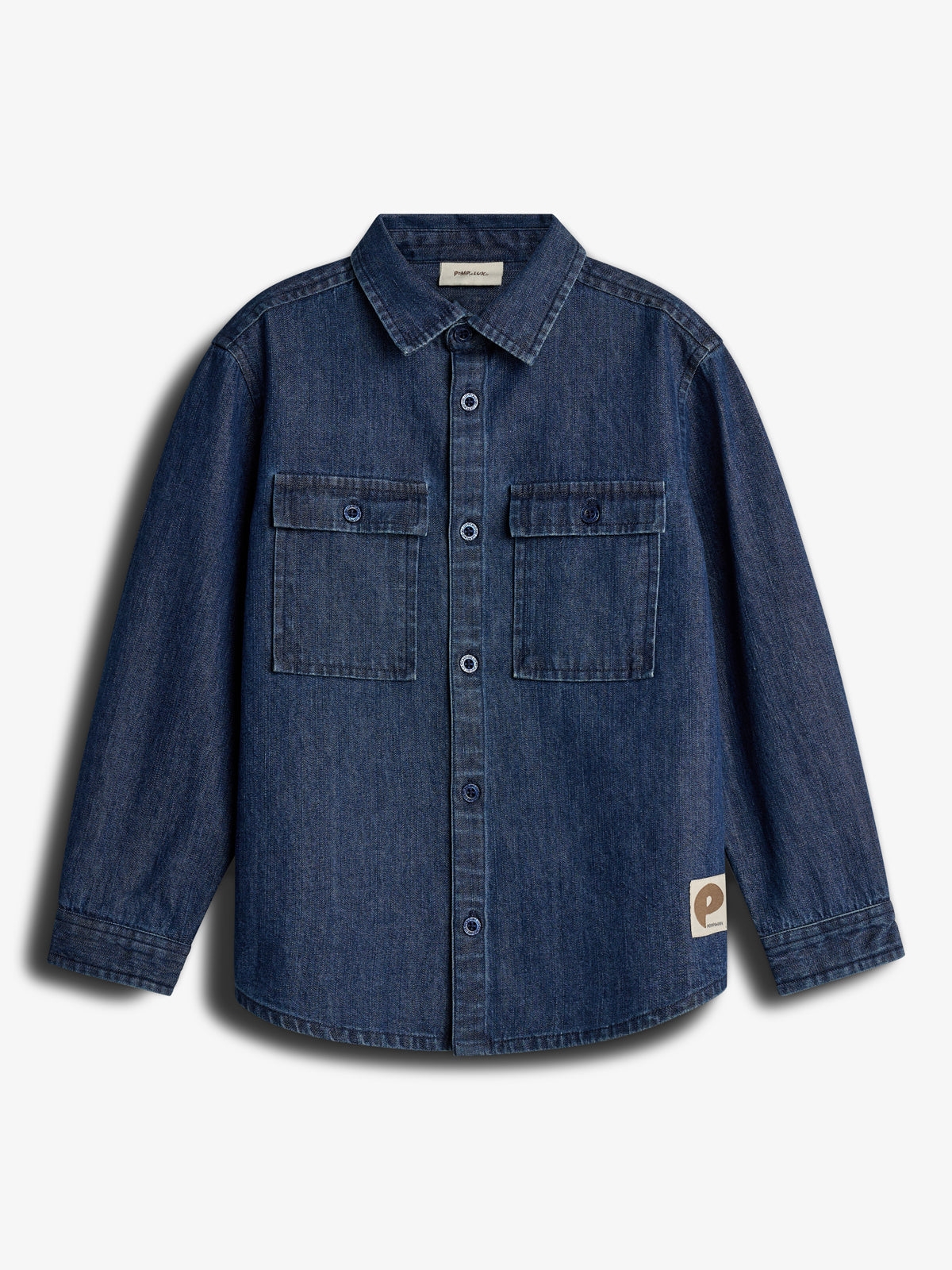 Denimskjorte med knapper og to brystlommer. Stiv krave og lange ærmer. Skjorten hænger mod en hvid baggrund. Et mærke nederst til højre viser teksten "Playwear".