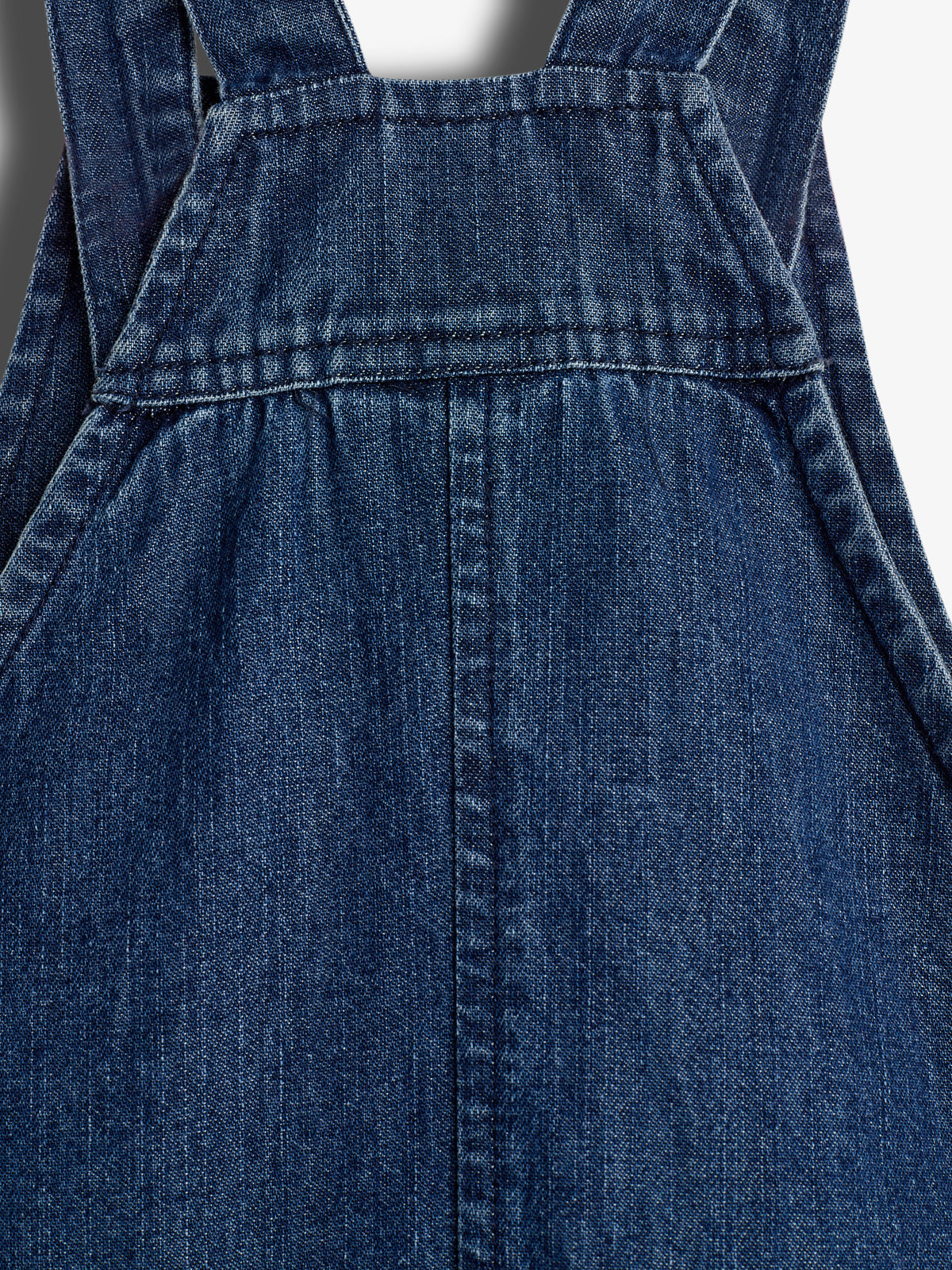 En mørkeblå denim overalls, hvor den øverste del ses med stropper og synlige søm detaljer. Stoffet er let struktureret i et tæt skud.