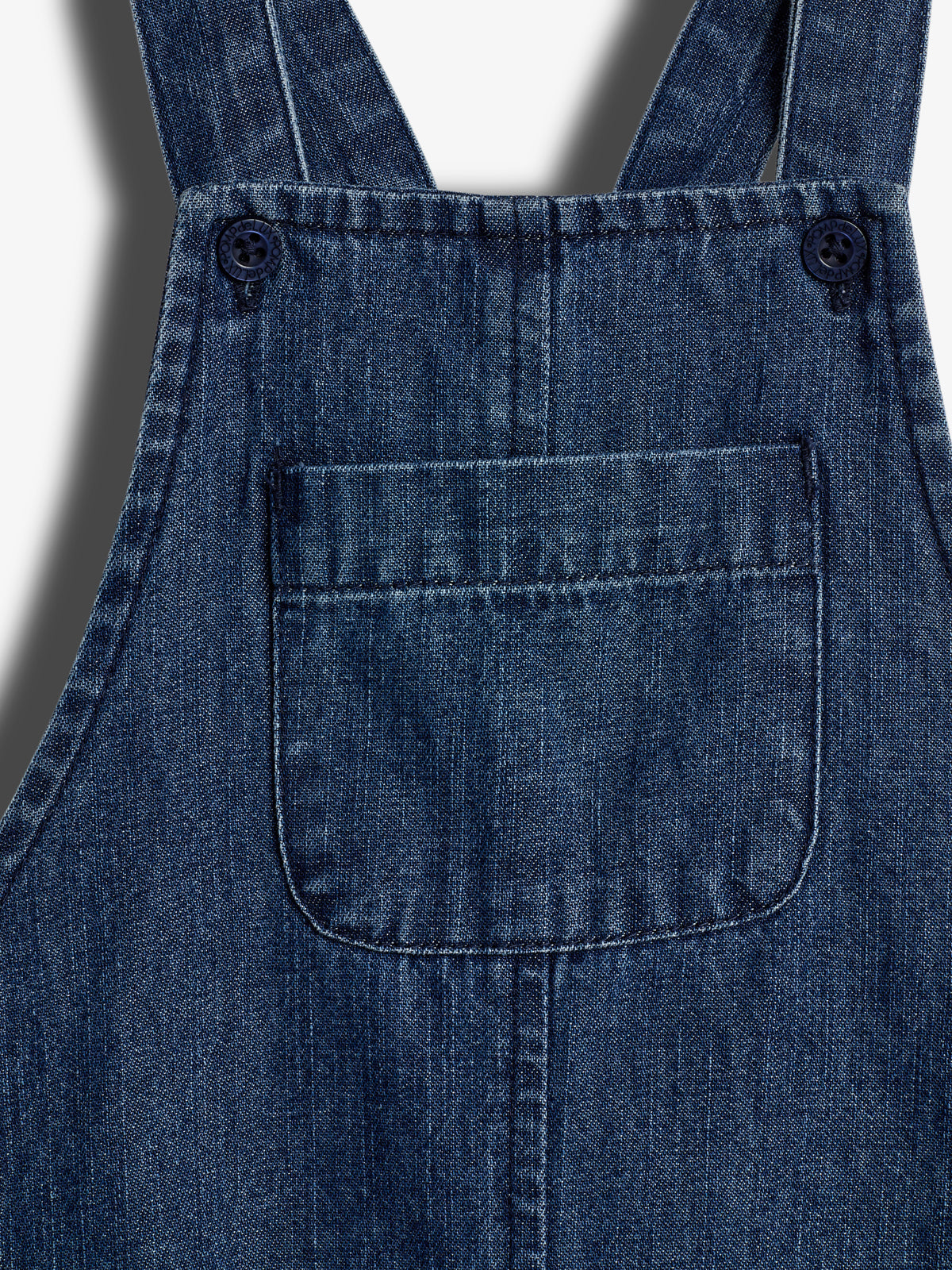 Jeansoverdel med en lomme, fastgjort med to knapper på stropperne, i et tekstureret denimstof.