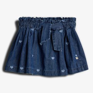 En denimnederdel med hjertebroderi, samlet i taljen og bundet med et bælte, mod en lys baggrund.