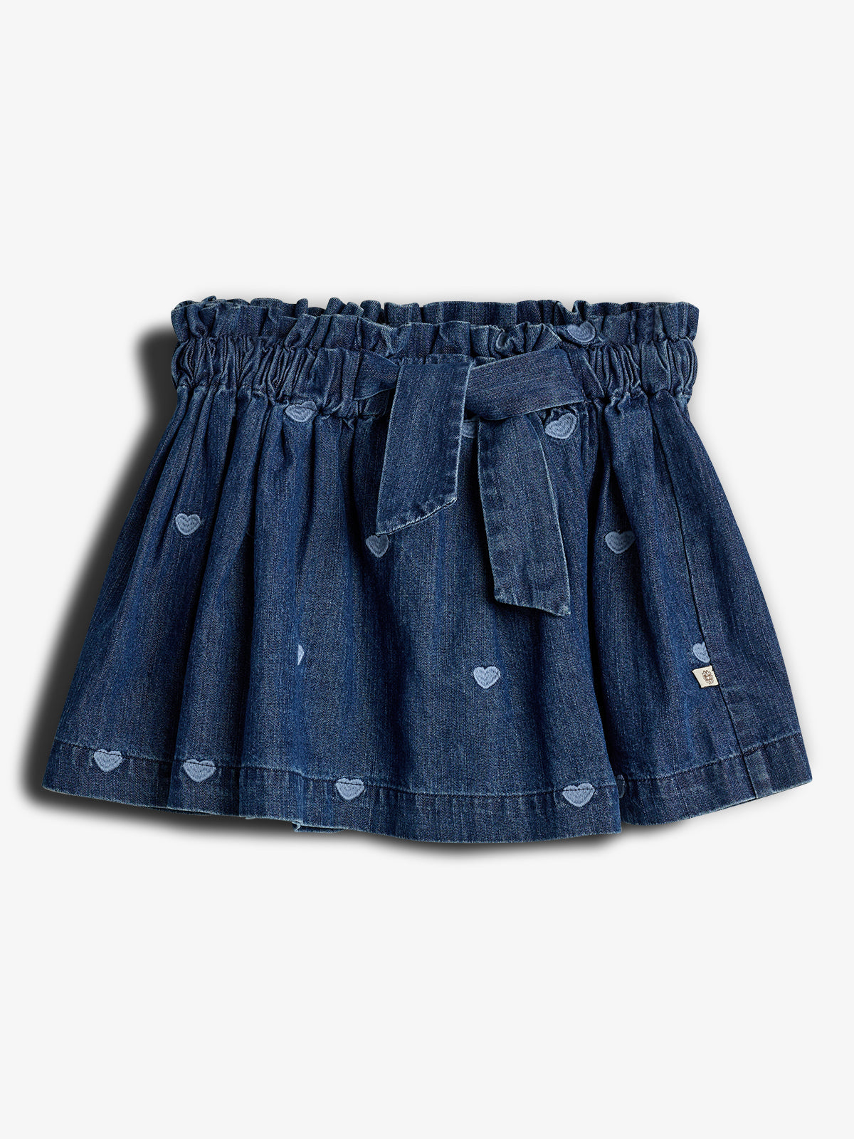 En denimnederdel med hjertebroderi, samlet i taljen og bundet med et bælte, mod en lys baggrund.