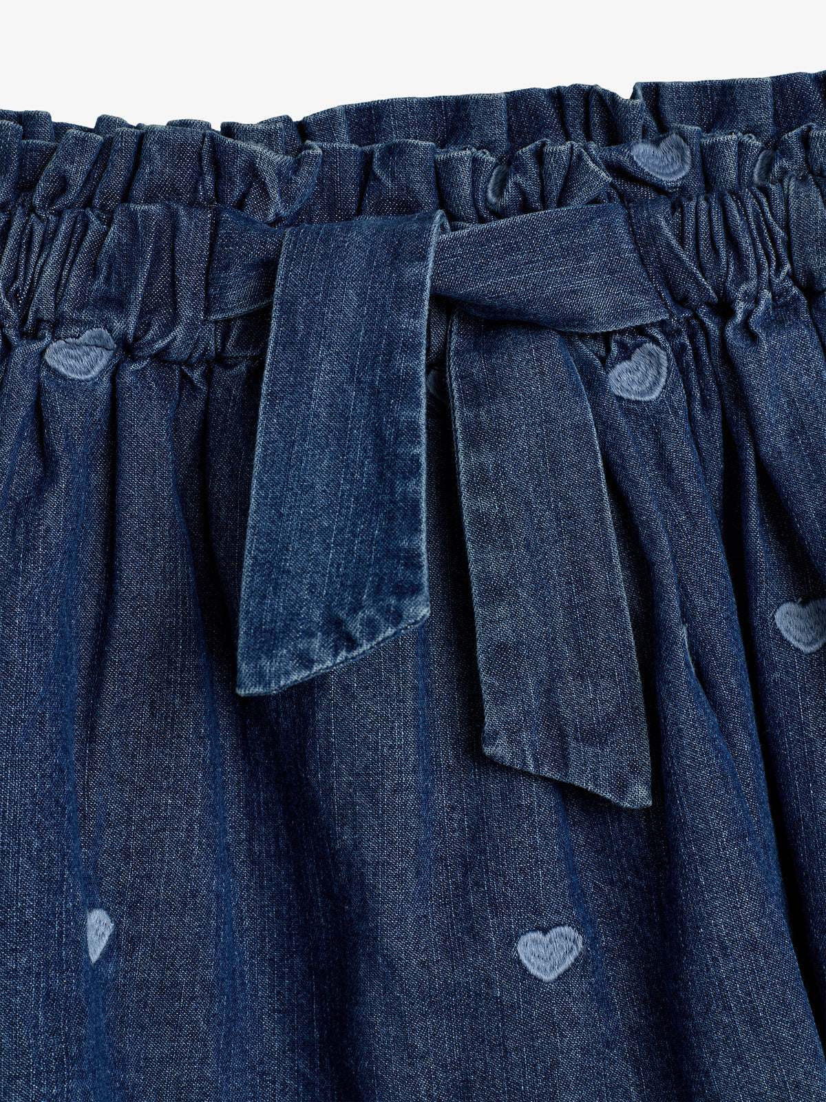 Elastisk denimskørt med påsyede hjerter og et bælte foran. Skørtet er i en dyb blå farve og har et afslappet design.