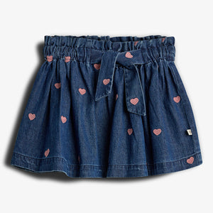 Nederdel i denim med lyserøde hjertebroderier, har en elastisk talje og bindebånd. Baggrund er enkel og hvid.